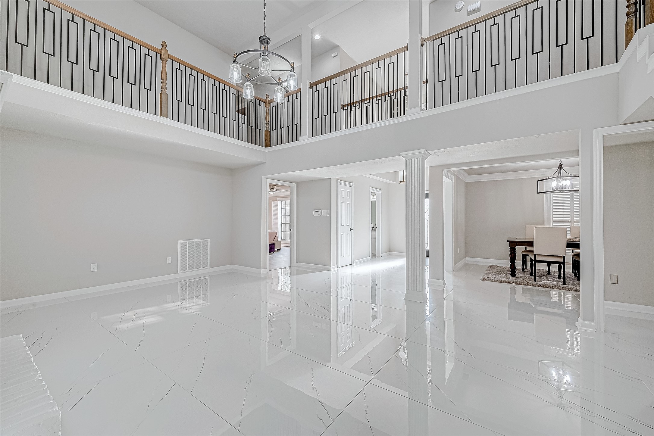 A bright open floor plan with high ceilings, elegant railing, and glossy white tile floors. A bright open floor plan with high ceilings, elegant railing, and glossy white tile floors.