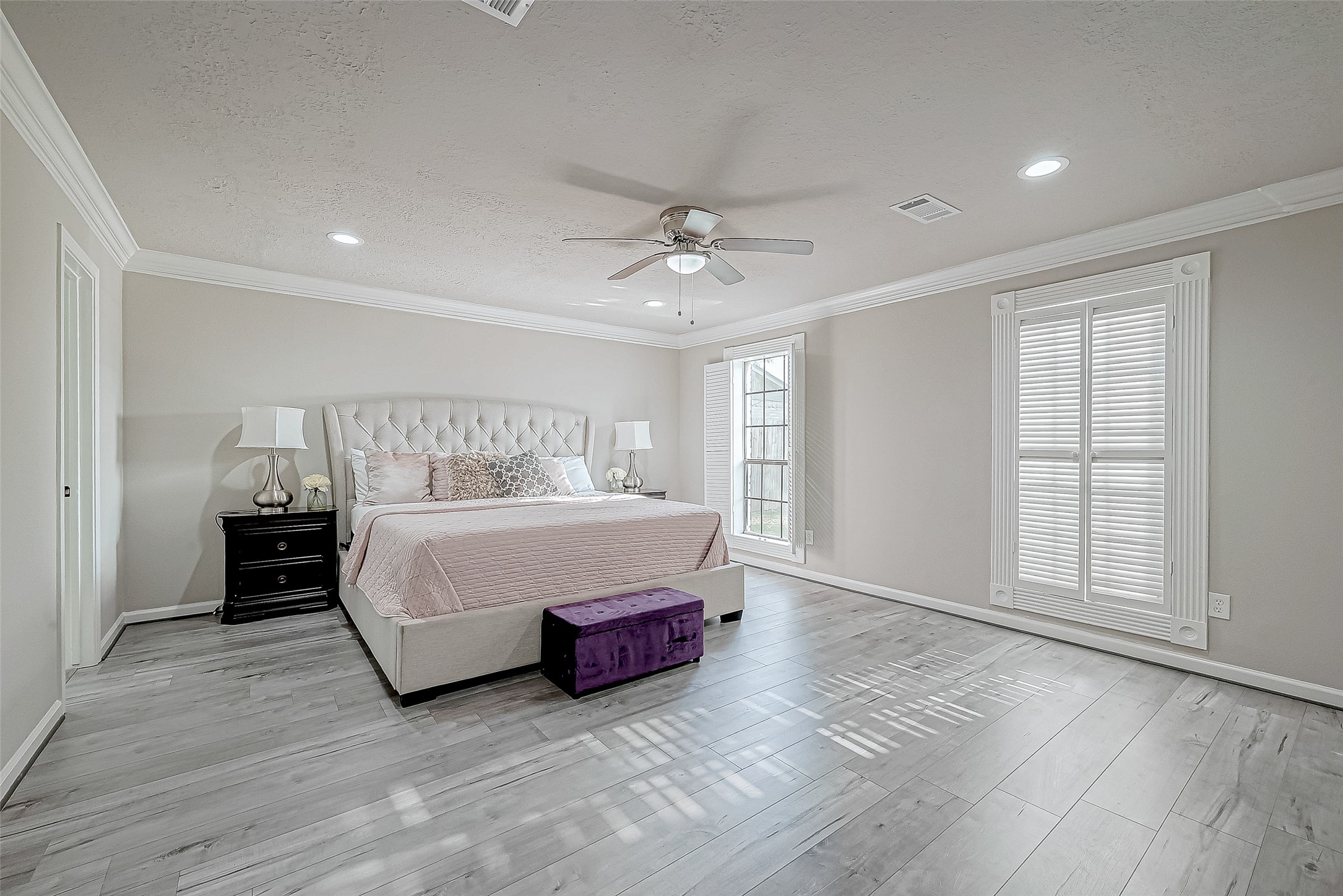 Primary bedroom features elegant hardwood floors, a cozy bed with a tufted headboard.