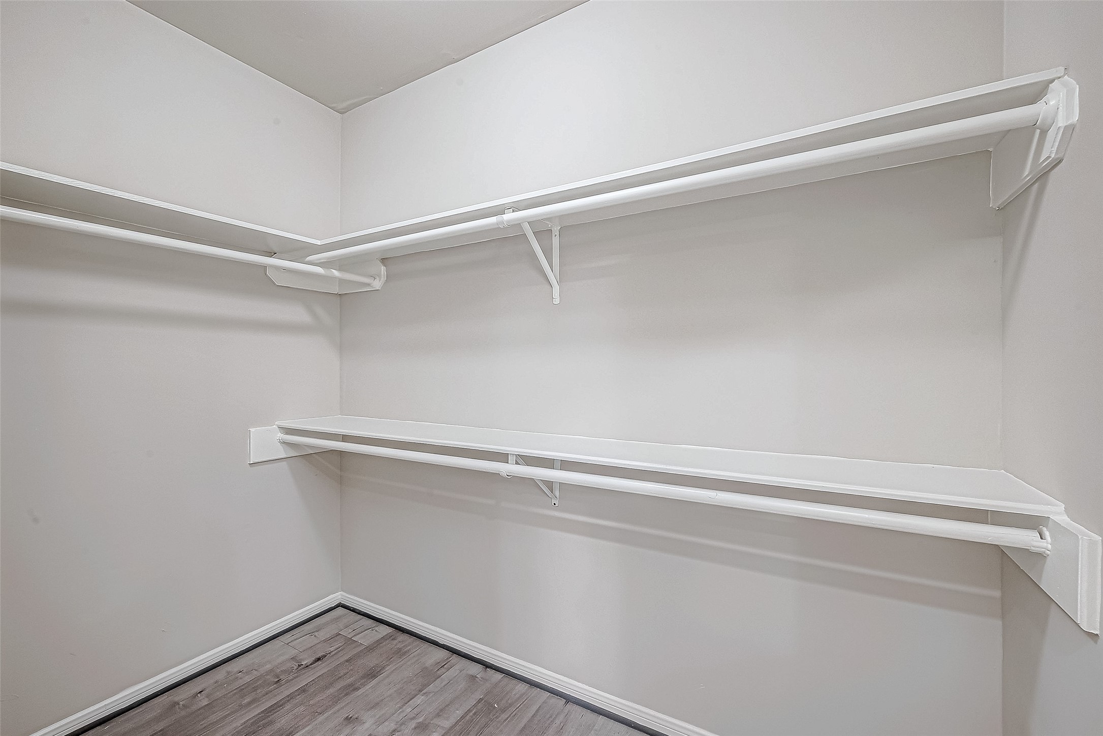 Walk-in closet features sleek wood flooring, dual-level white shelving, and ample hanging rods for optimal organization.