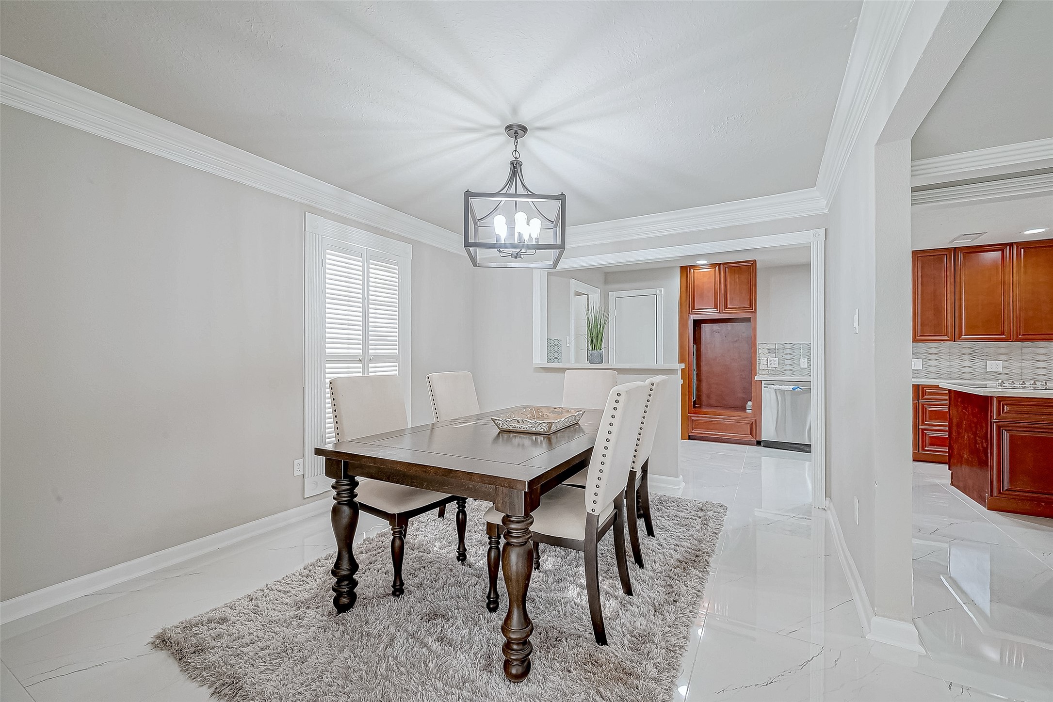 The dining area features elegant crown molding, a chandelier, and neutral tones. It includes a wooden dining table with upholstered chairs. The dining area features elegant crown molding, a chandelier, and neutral tones. It includes a wooden dining table with upholstered chairs.