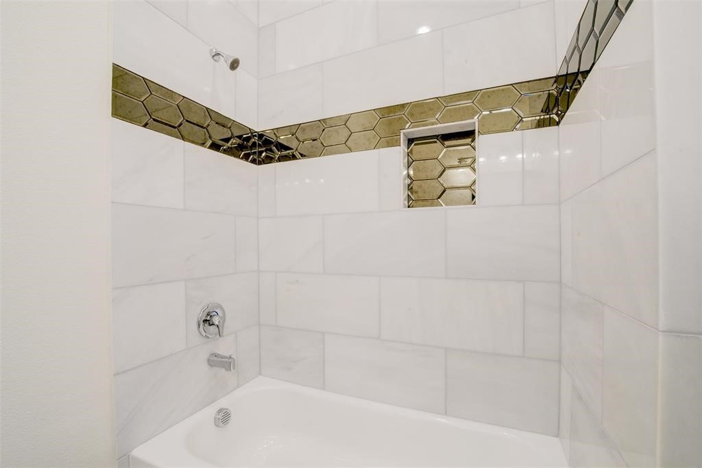 This bathroom features a modern tub and shower combination with sleek white tiles, accented by a stylish horizontal strip of hexagonal tiles. There's a recessed shelf for convenient storage.