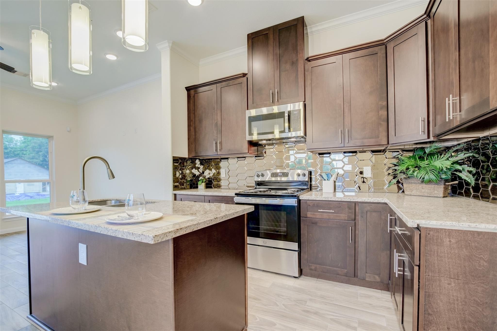 Gorgeous Kitchen features modern dark wood cabinets, stainless steel appliances, and a stylish hexagonal tile backsplash. The island offers additional counter space and seating, complemented by pendant lighting for a bright, inviting atmosphere.
