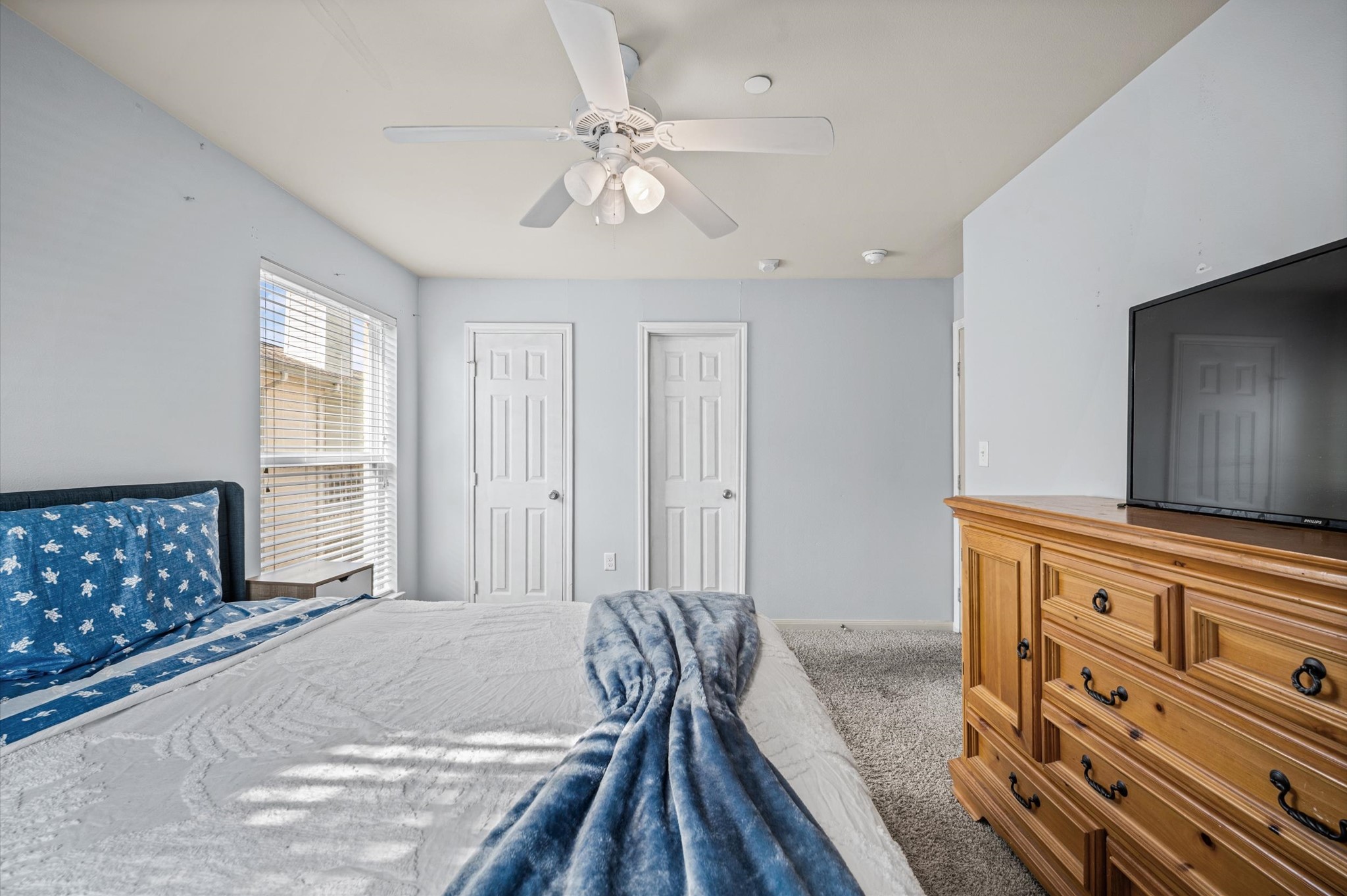 Cozy bedroom with soft carpeting, a ceiling fan, and abundant natural light from large windows.