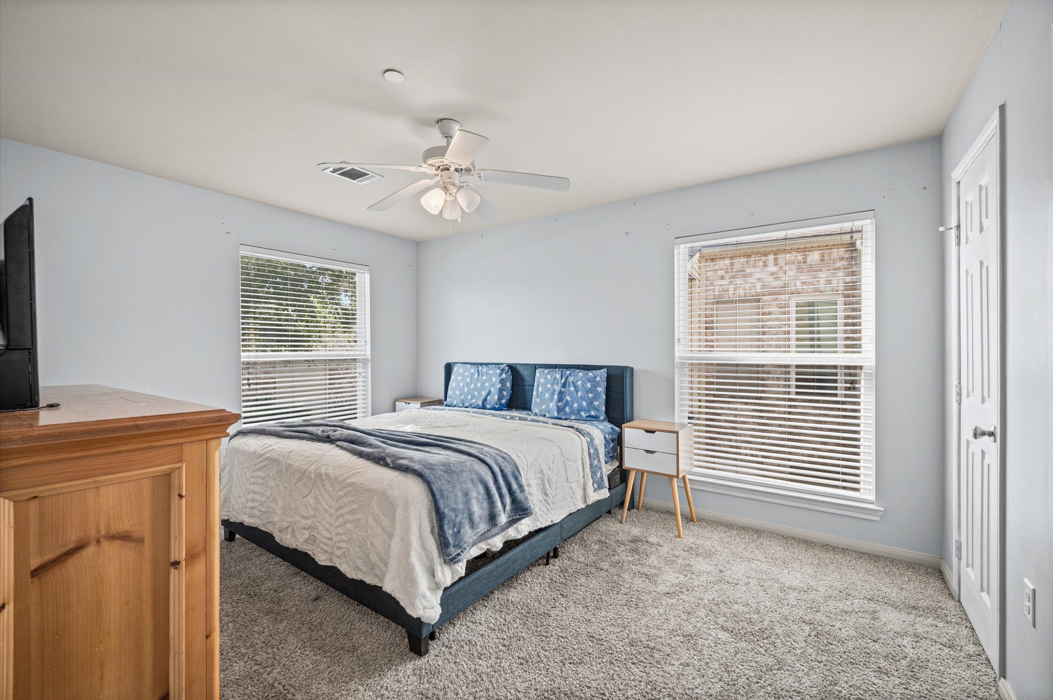 Spacious bedroom with large windows that fill the space with natural light, featuring a cozy carpeted floor and a ceiling fan for added comfort.