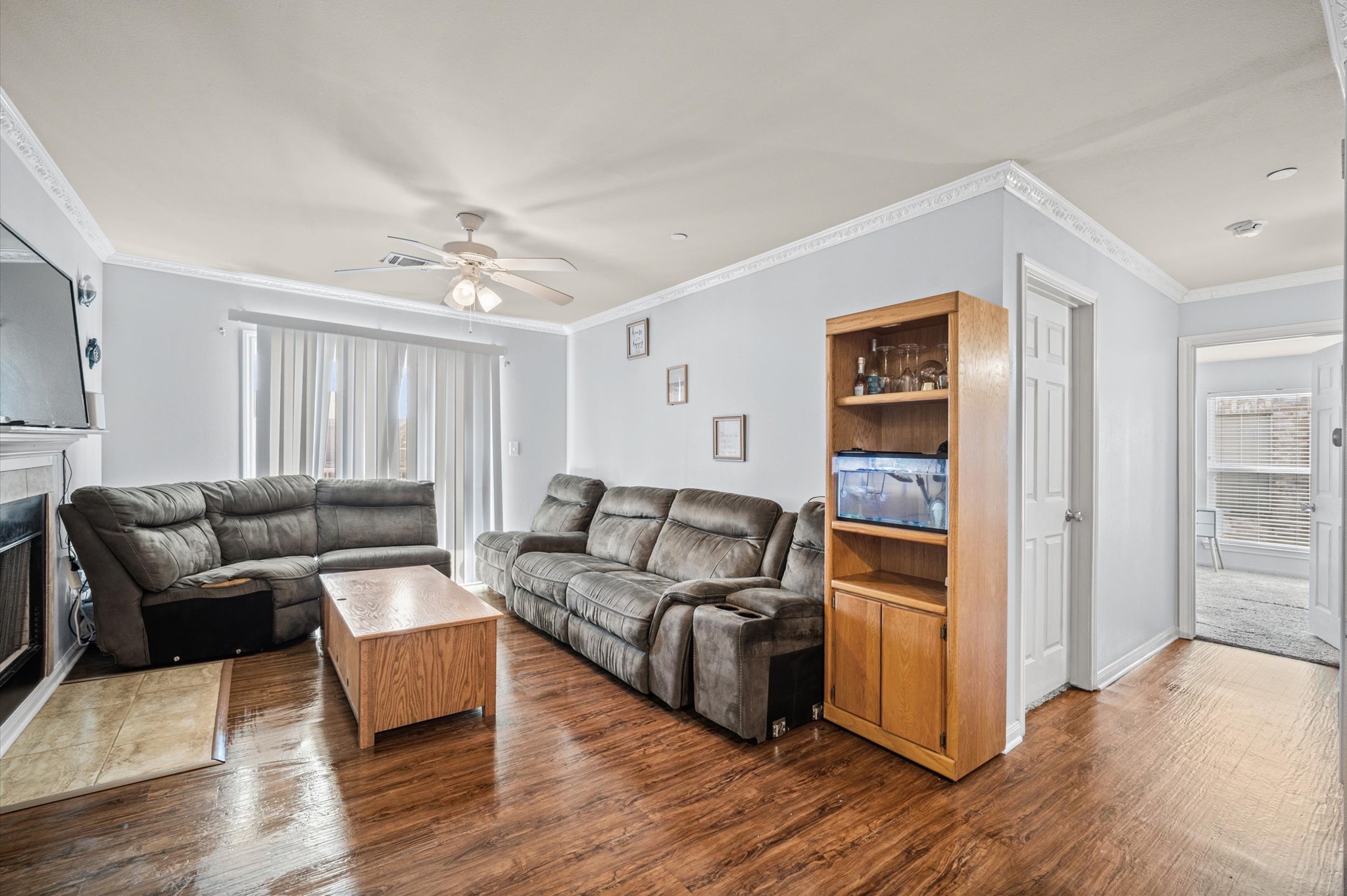 Spacious living room with hardwood floors, cozy living space, and a ceiling fan for comfort. Natural light fills the room through large sliding doors, and a charming fireplace adds warmth and ambiance.