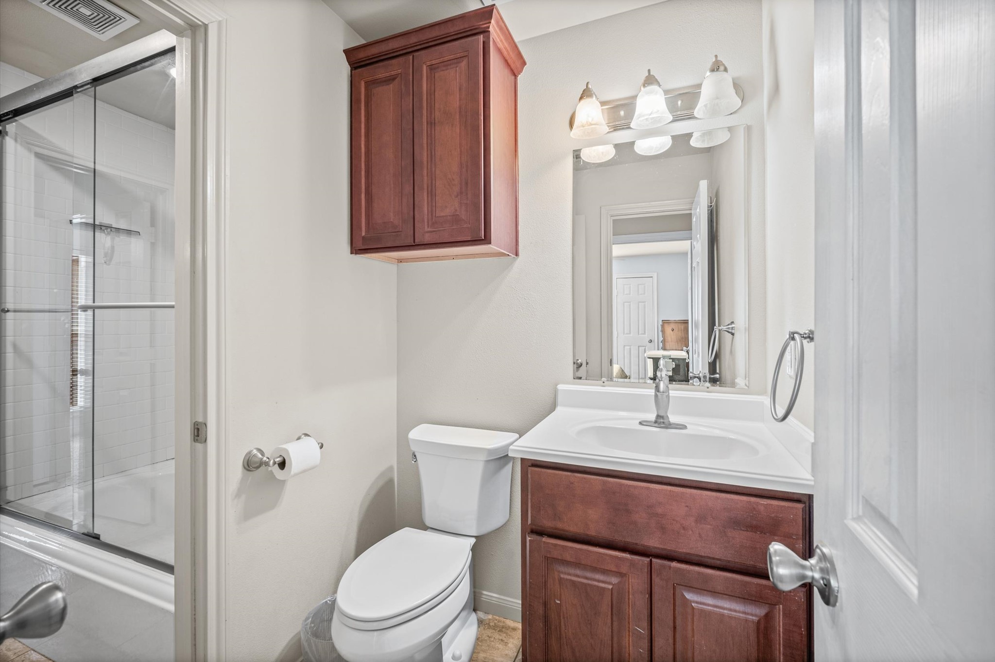 Charming bathroom featuring a sleek glass-enclosed shower, elegant vanity with ample storage, and warm wooden cabinetry.