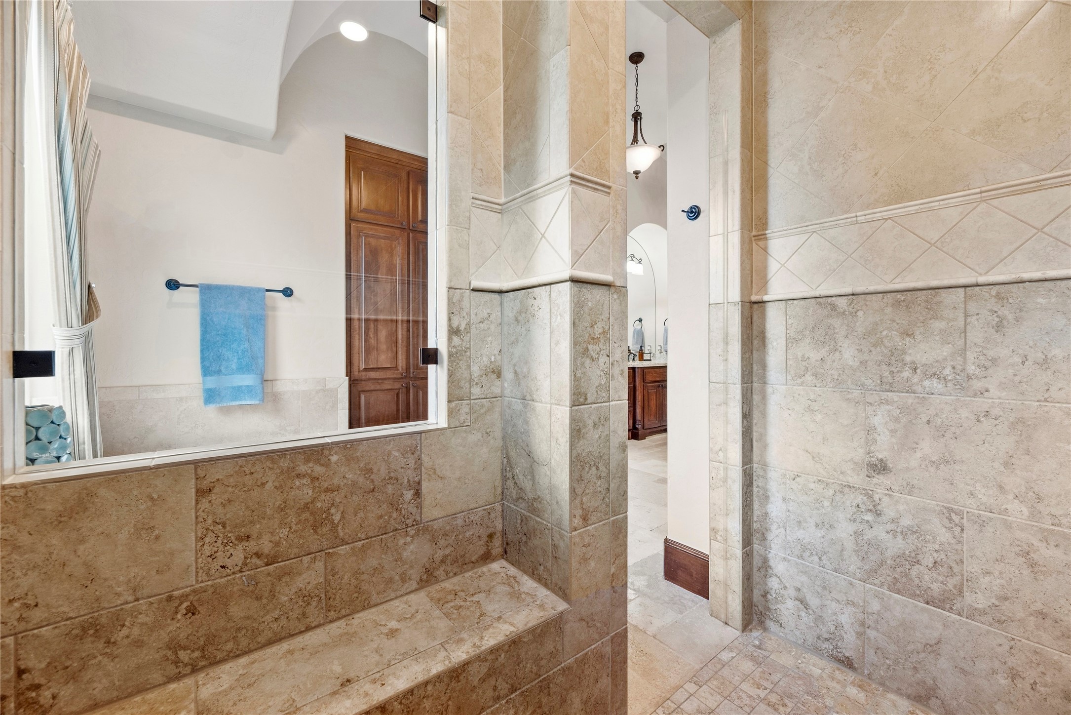 Shower is tucked in the corner with a bench and a view of that awesome bathroom