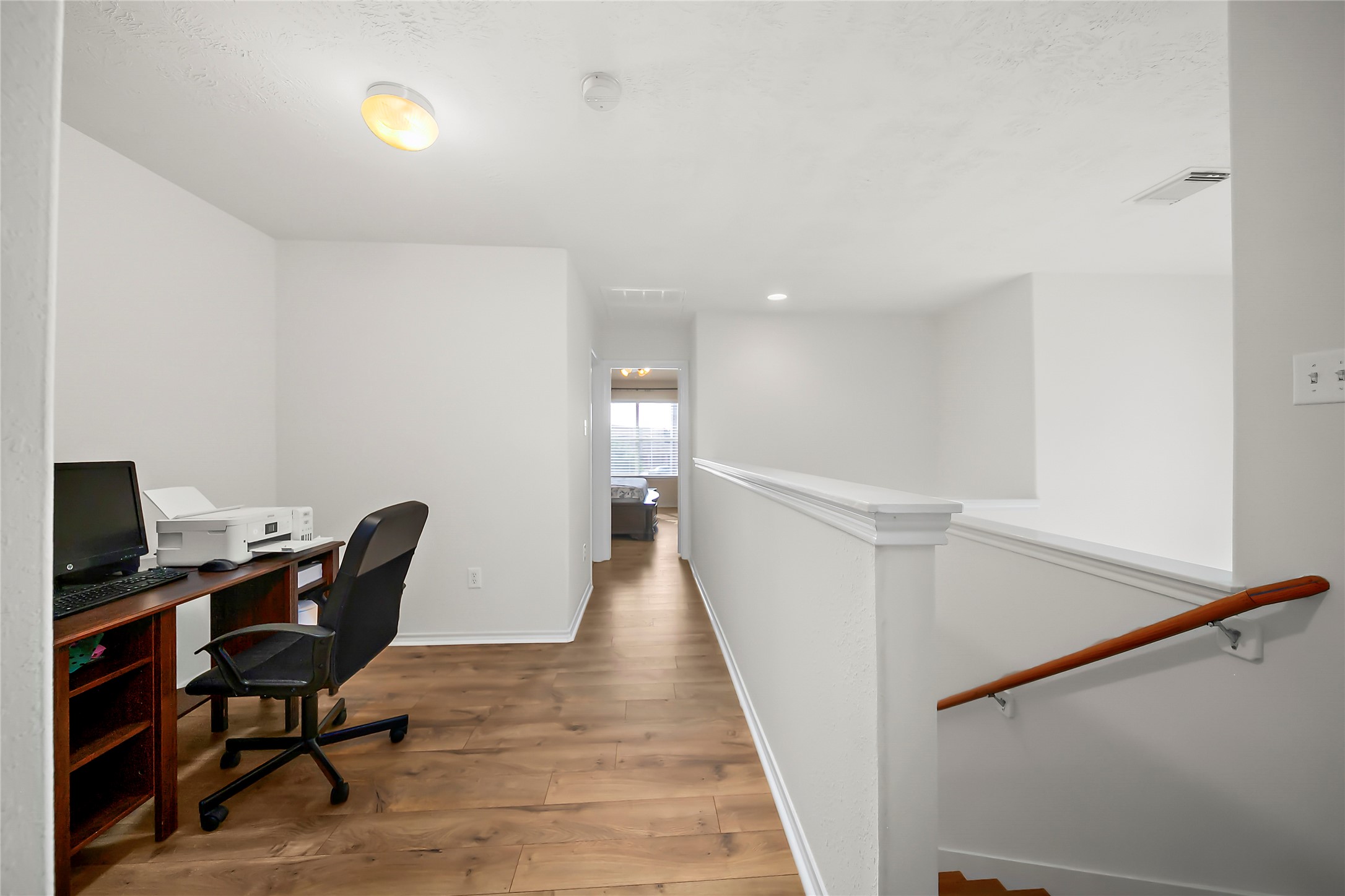 Bright dining and living area with natural light, featuring a rustic wooden table, cozy seating, and a piano. Large windows and a door open to the outside, enhancing the airy feel.