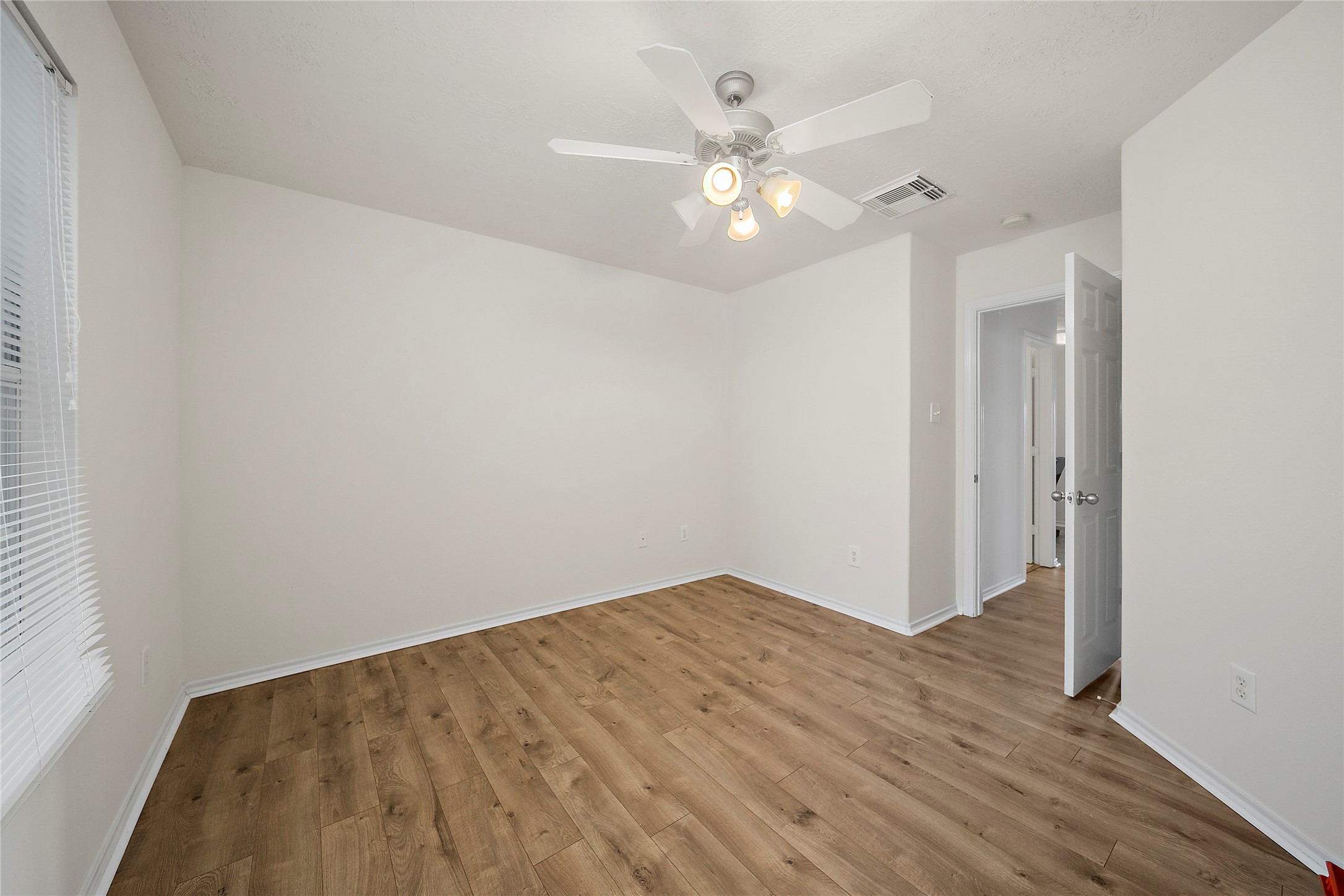 This photo shows a bright, open-concept living area with a blend of hardwood and tile flooring. The kitchen features ample white cabinetry and modern appliances, while the adjacent space is perfect for dining or lounging. A ceiling fan and built-in shelving add functionality and comfort.