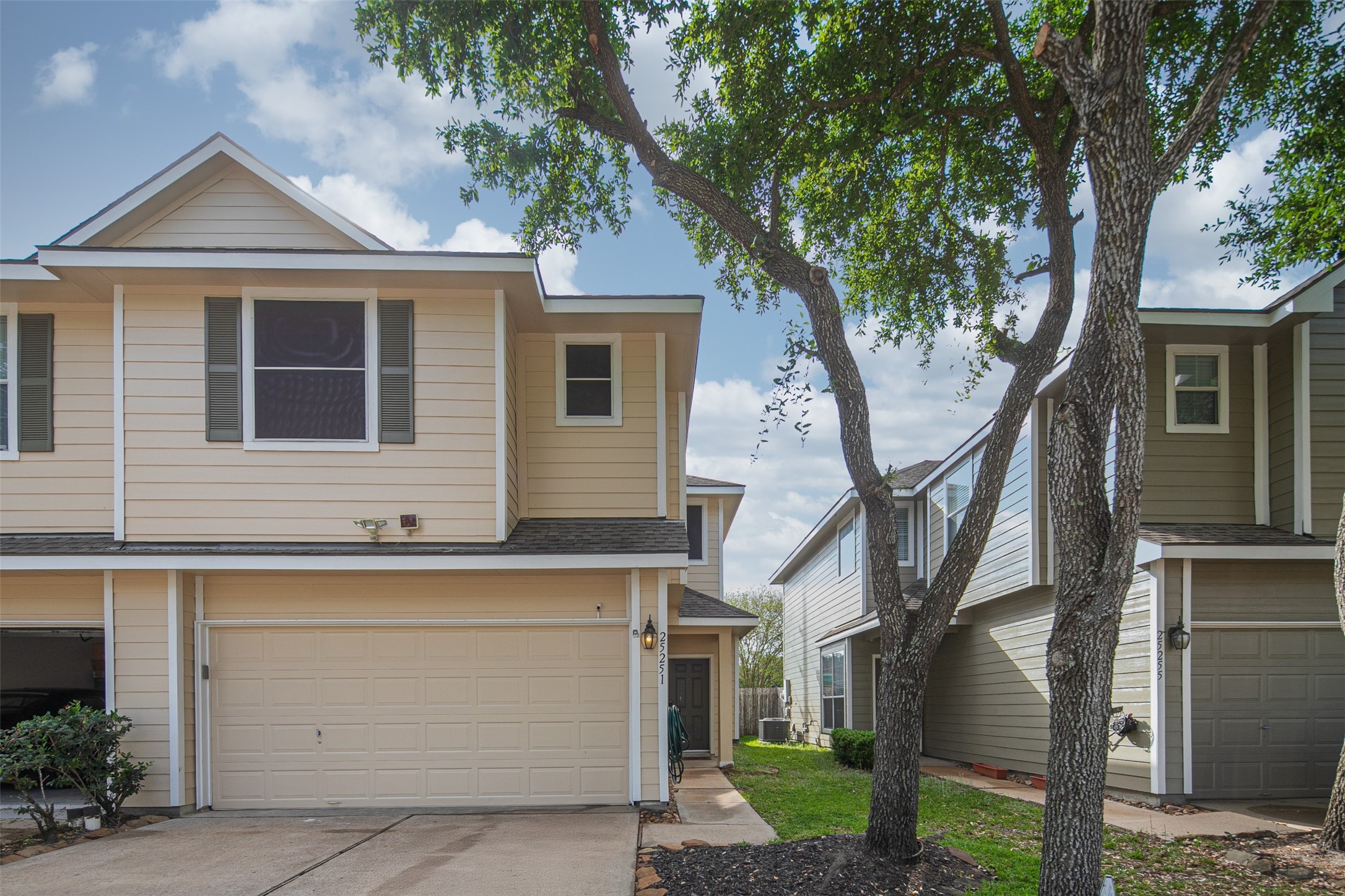 Charming two-story home with a spacious two-car garage and a welcoming front yard shaded by mature trees.