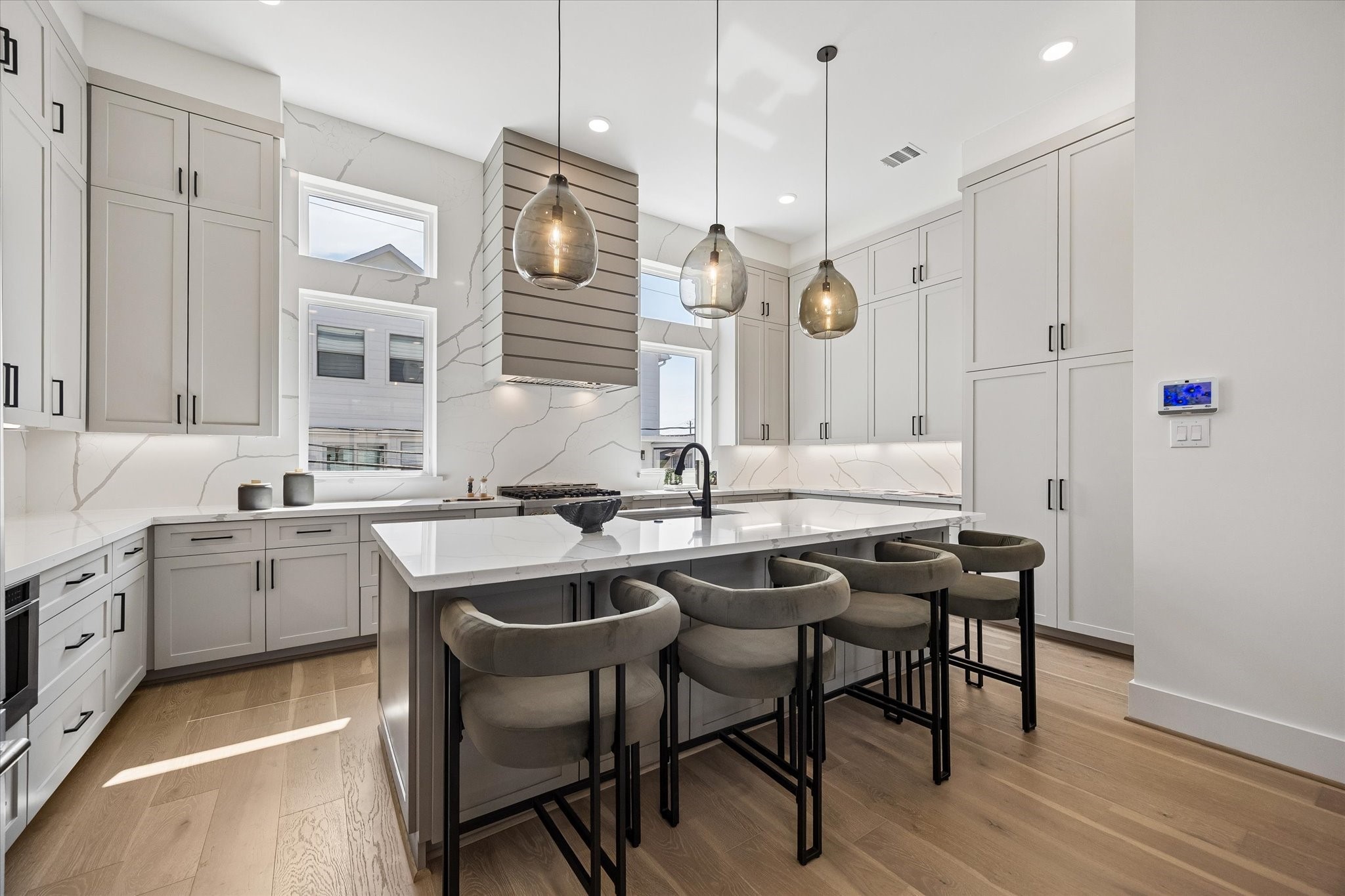 Another view of this stunning kitchen equipped w/ ample storage w/ custom-cabinetry built to the ceiling and large double door pantry.  Custom touches w/ pull-out spice racks and cookie tray divider. Natural light floods in through two large windows, beautifully complemented by Visual Comfort pendants and recessed lighting.