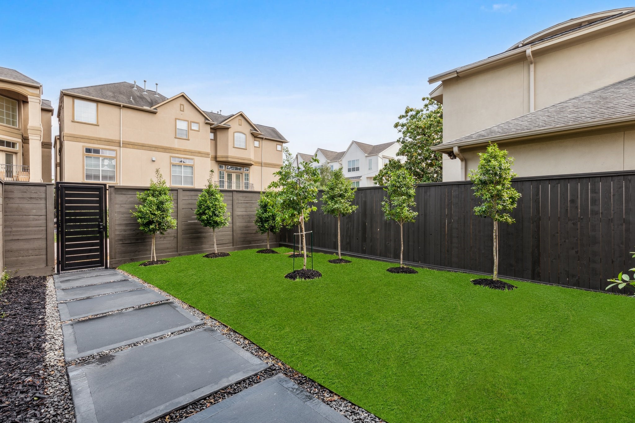 Another view of the spacious yard, framed by a cedar wood fence and a custom iron front door. A colored concrete walkway adds curb appeal as it leads you to the elegant entry.  Note: grass has been edited.