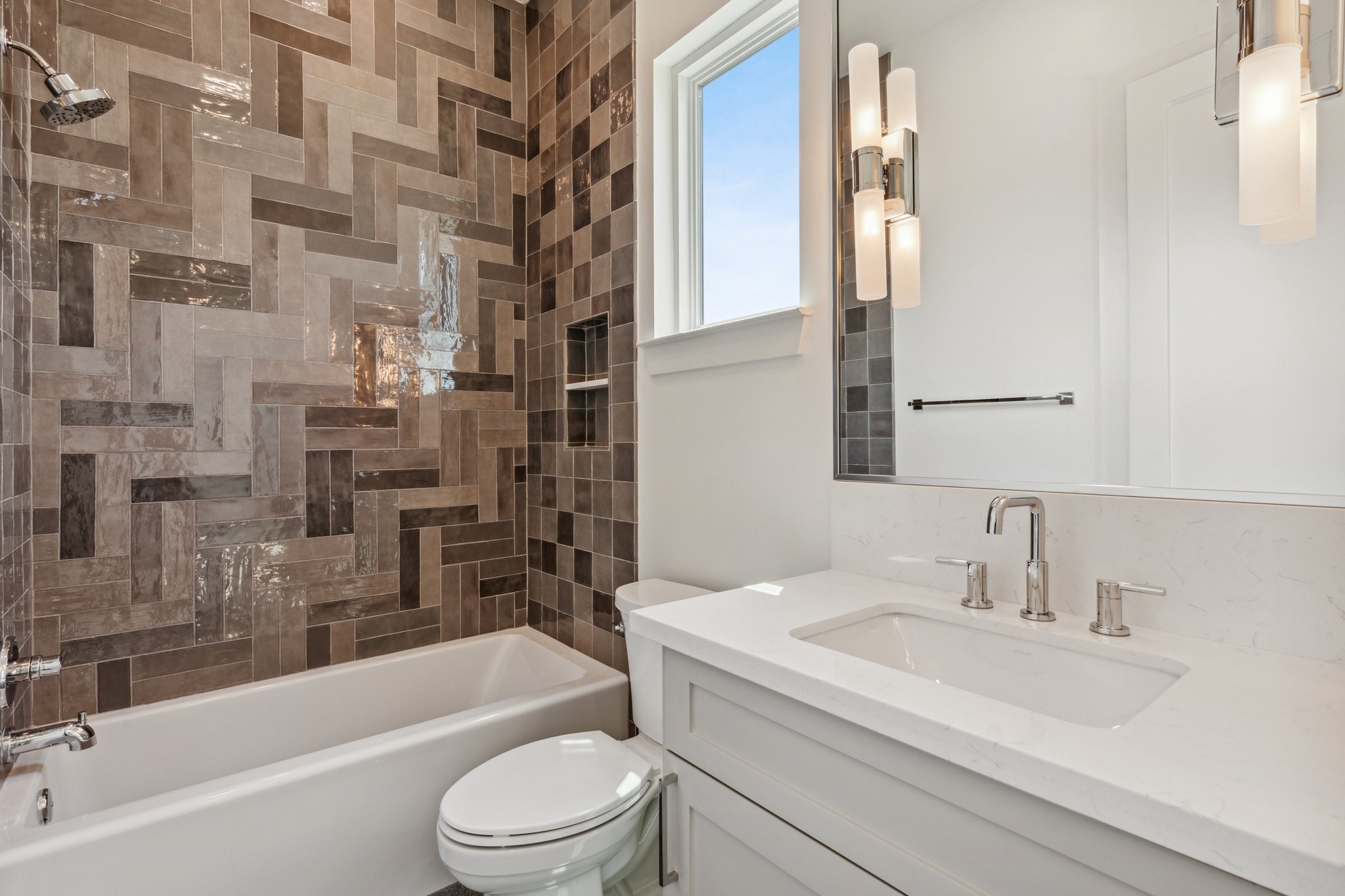 This stylish ensuite bathroom for secondary bedroom #1 on the 3rd floor, features sleek 24x48 porcelain tile floors, a custom-built vanity with pull-out shelves, quartz countertop, and Top Knob hardware. Enjoy the spacious walk-in closet with dresser, while the tub/shower combo with decorative tile wall adds a touch of elegance. Visual Comfort sconces and a Kohler toilet complete the refined space.