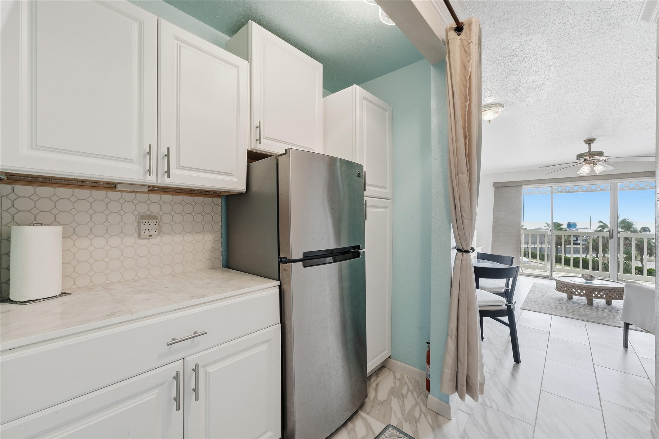 Kitchen with white cabinetry and a stainless refrigerator, open to the living area
