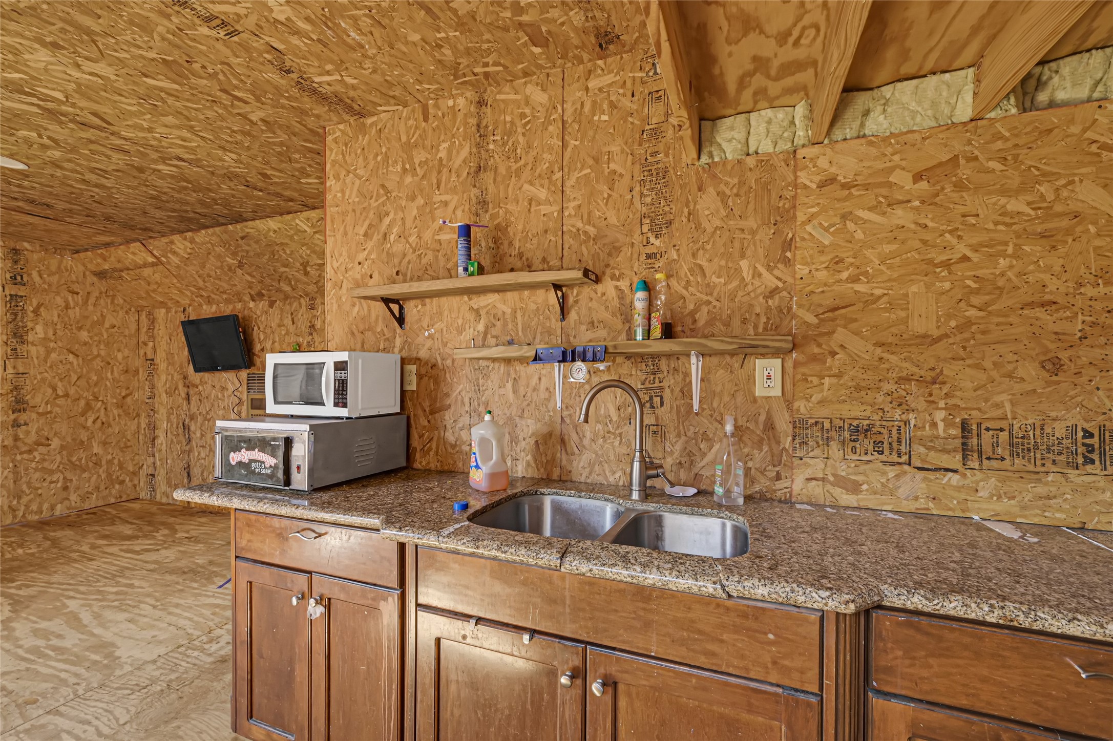 Rustic kitchen space featuring wood paneling, granite countertops, a double sink, and open shelving for convenience.