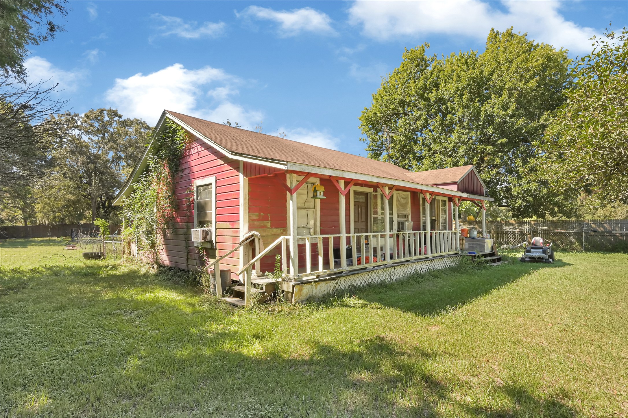 Charming red cottage with a welcoming front porch, nestled in a spacious yard surrounded by mature trees.