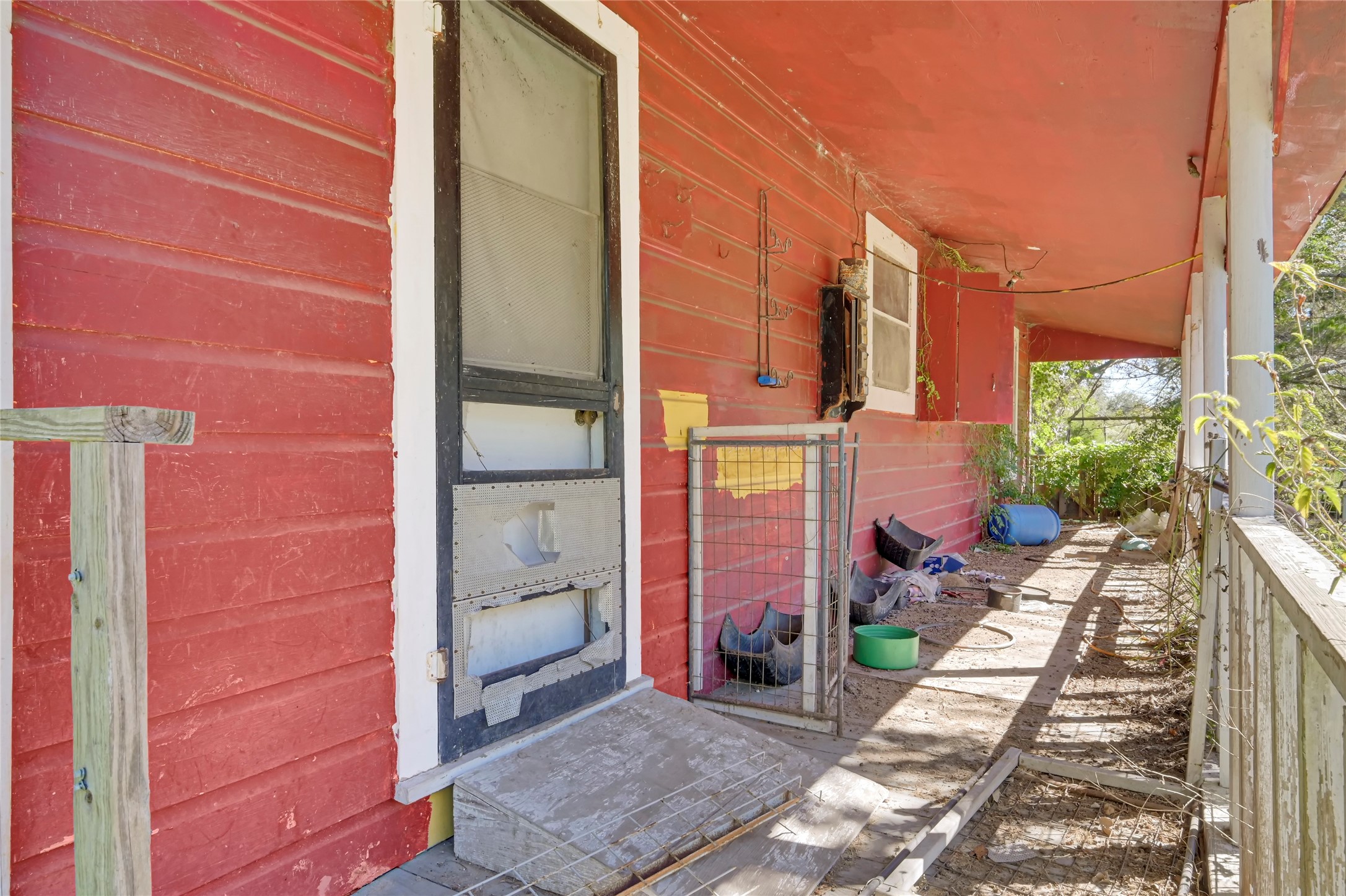 Charming rustic porch with vibrant red siding, offering a cozy outdoor space surrounded by lush greenery, perfect for relaxation or creative renovation.