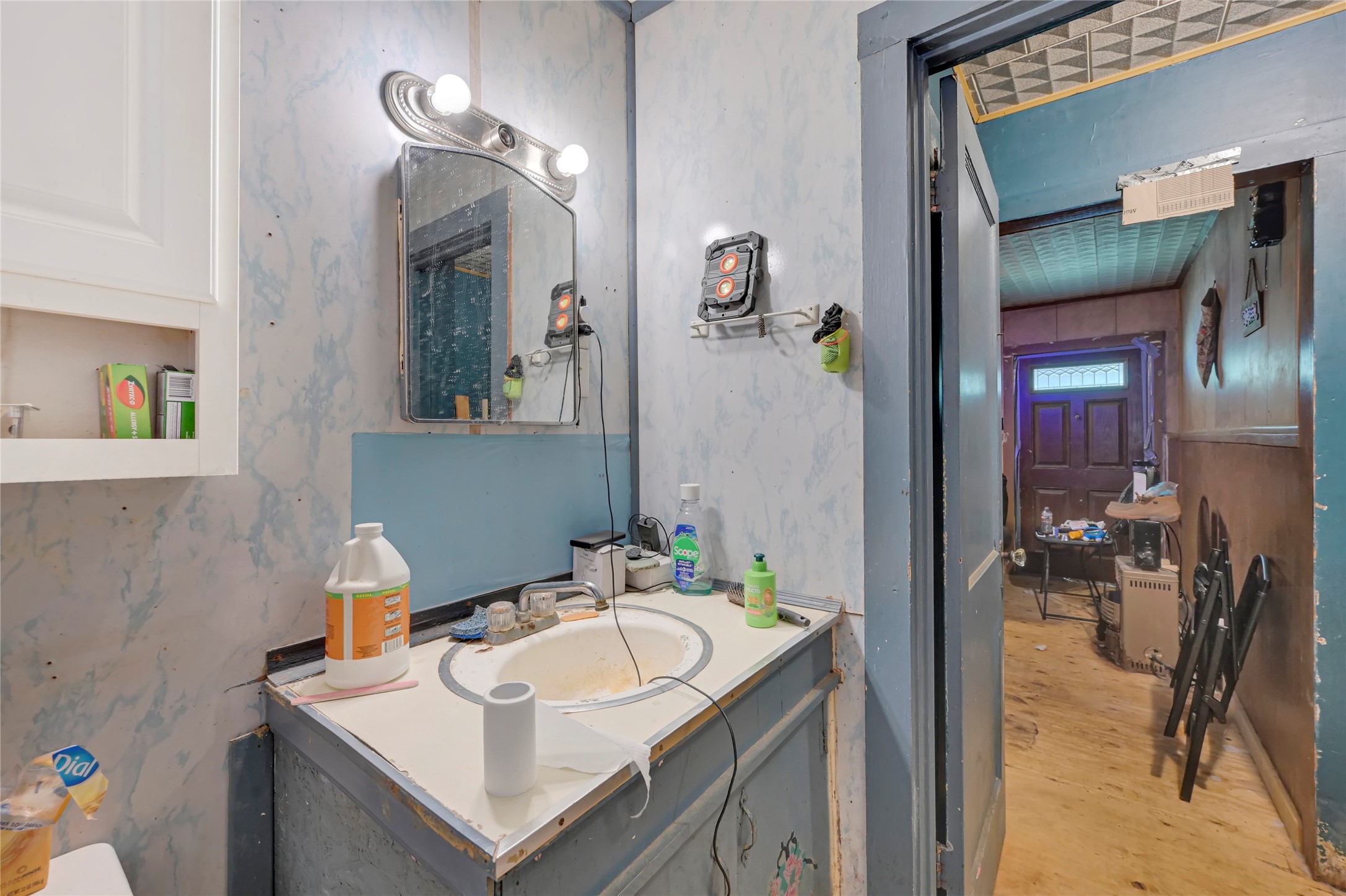 Cozy bathroom with a vintage vibe features a large mirror, ample lighting, and classic cabinetry, leading into a rustic hallway.