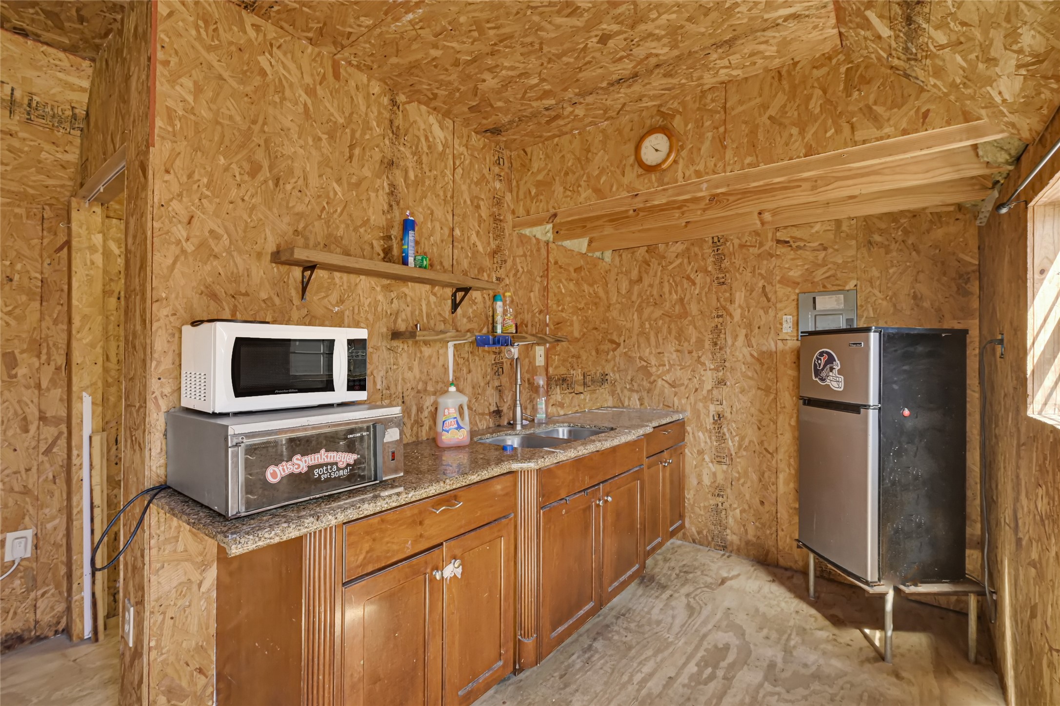 Cozy kitchenette with rustic wood paneling, featuring a compact fridge, microwave, and countertop oven, offering functional space for meal prep.