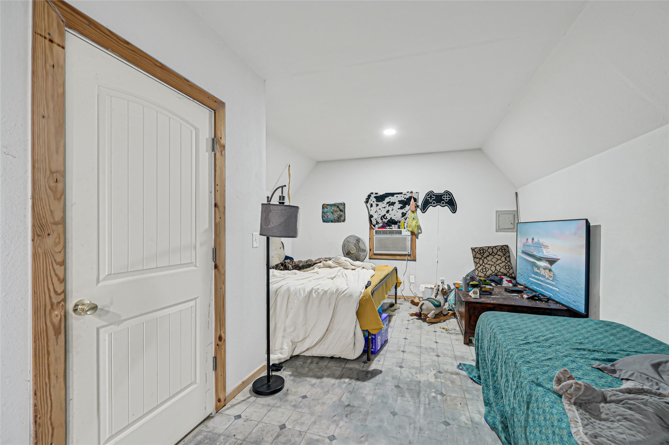 Cozy bedroom with sloped ceilings, featuring a bed, a TV, and a window air conditioner for climate control.