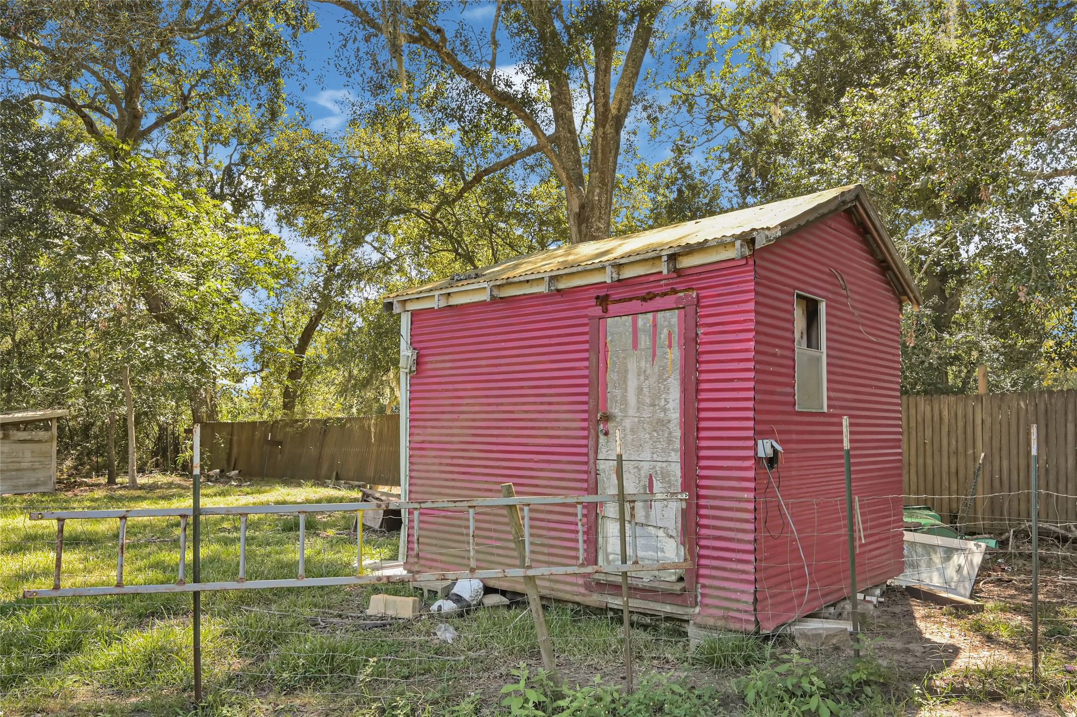 Charming rustic shed with vibrant pink siding set amidst a lush, fenced backyard, offering potential for creative outdoor projects.