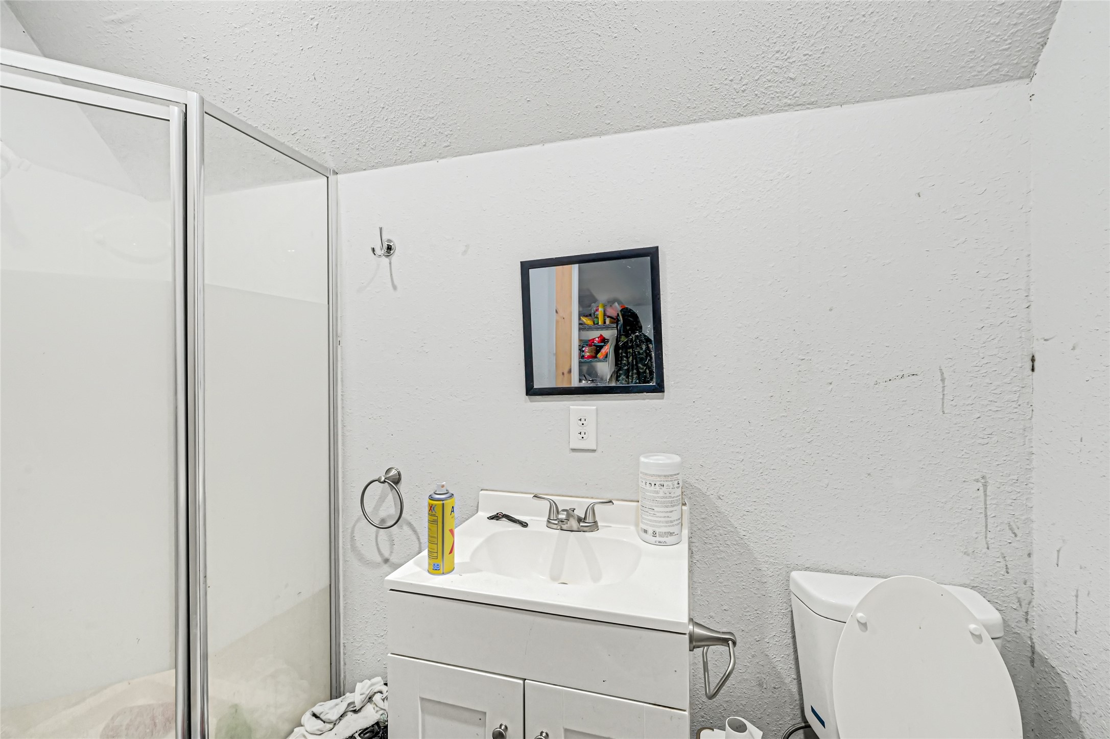 Compact bathroom featuring a corner shower with glass doors, a vanity with storage, and a wall-mounted mirror.