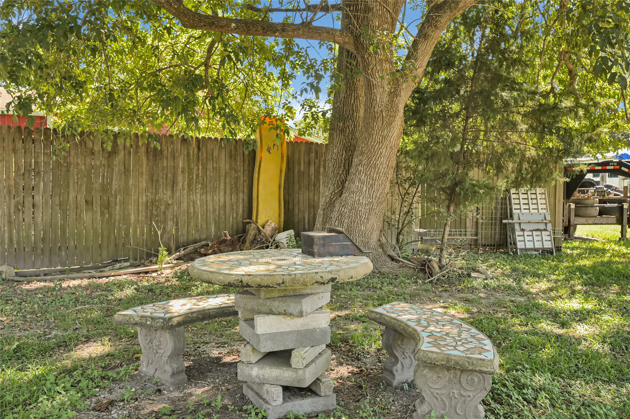 Charming backyard retreat with a mosaic stone table and benches under the shade of mature trees, perfect for relaxing and enjoying nature.