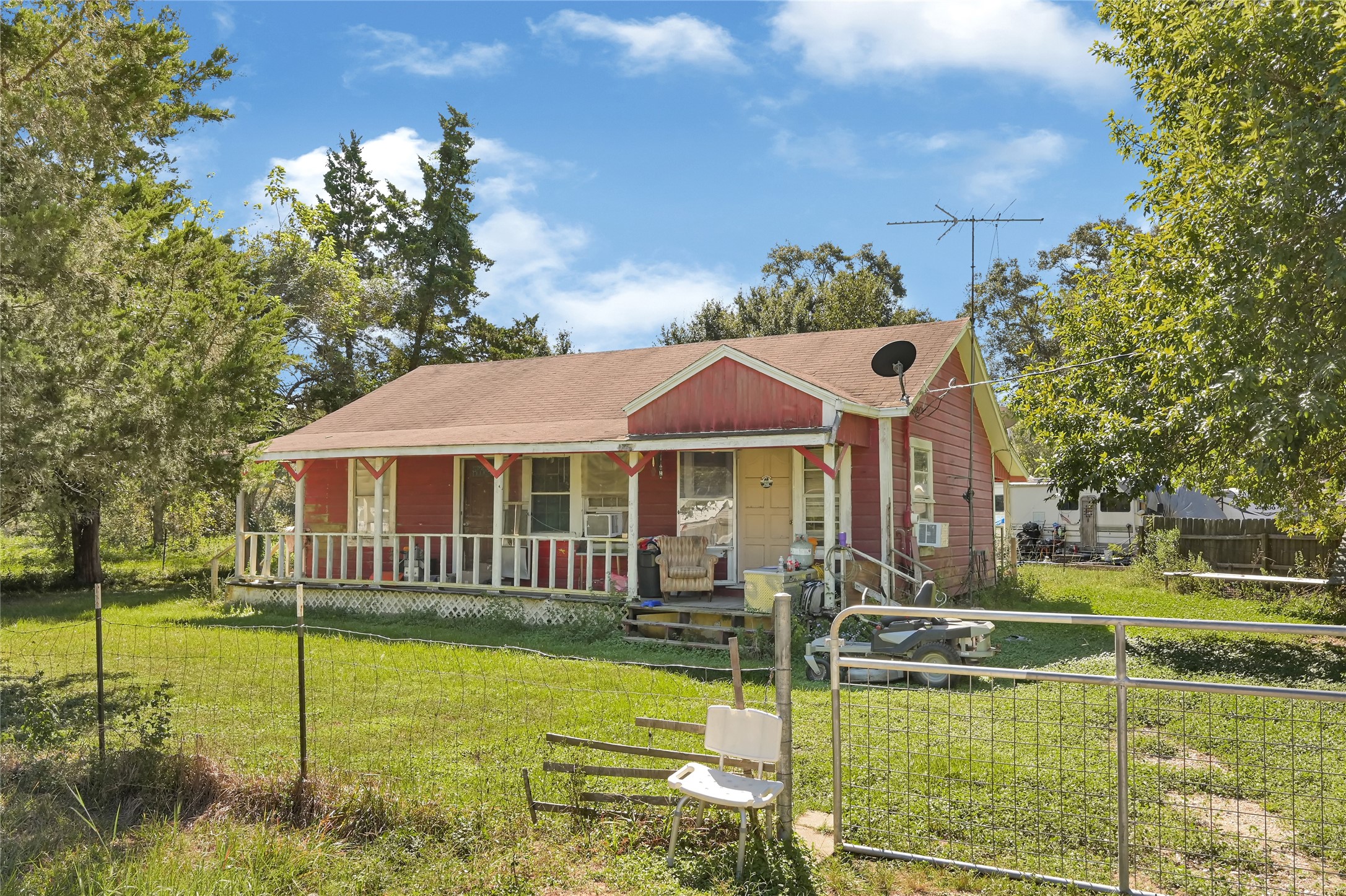Charming country home with a welcoming front porch, nestled amid mature trees and lush greenery, perfect for enjoying serene outdoor moments.