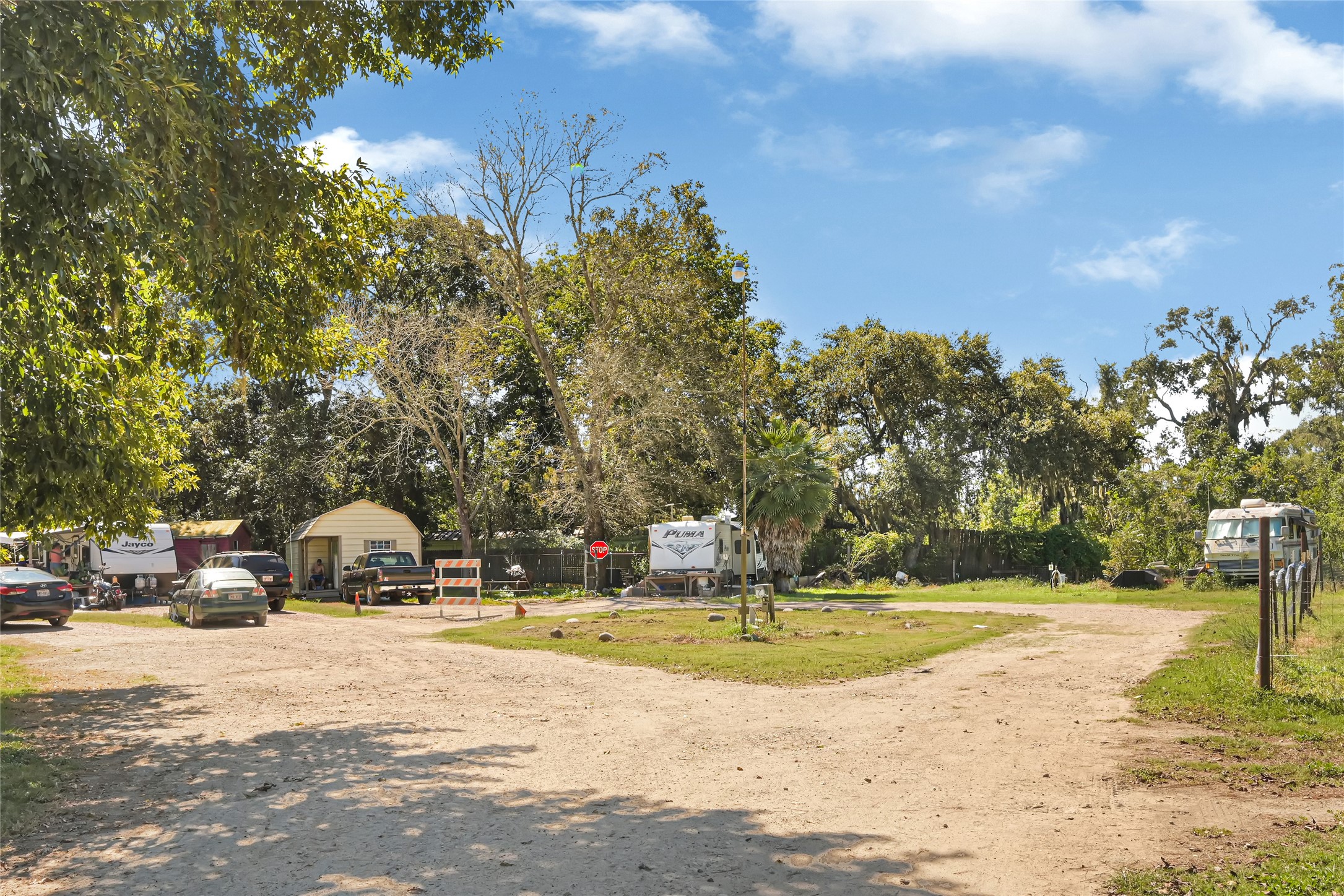 Spacious outdoor area with mature trees, multiple vehicles, and RVs, offering a rustic setting ideal for flexible living arrangements.