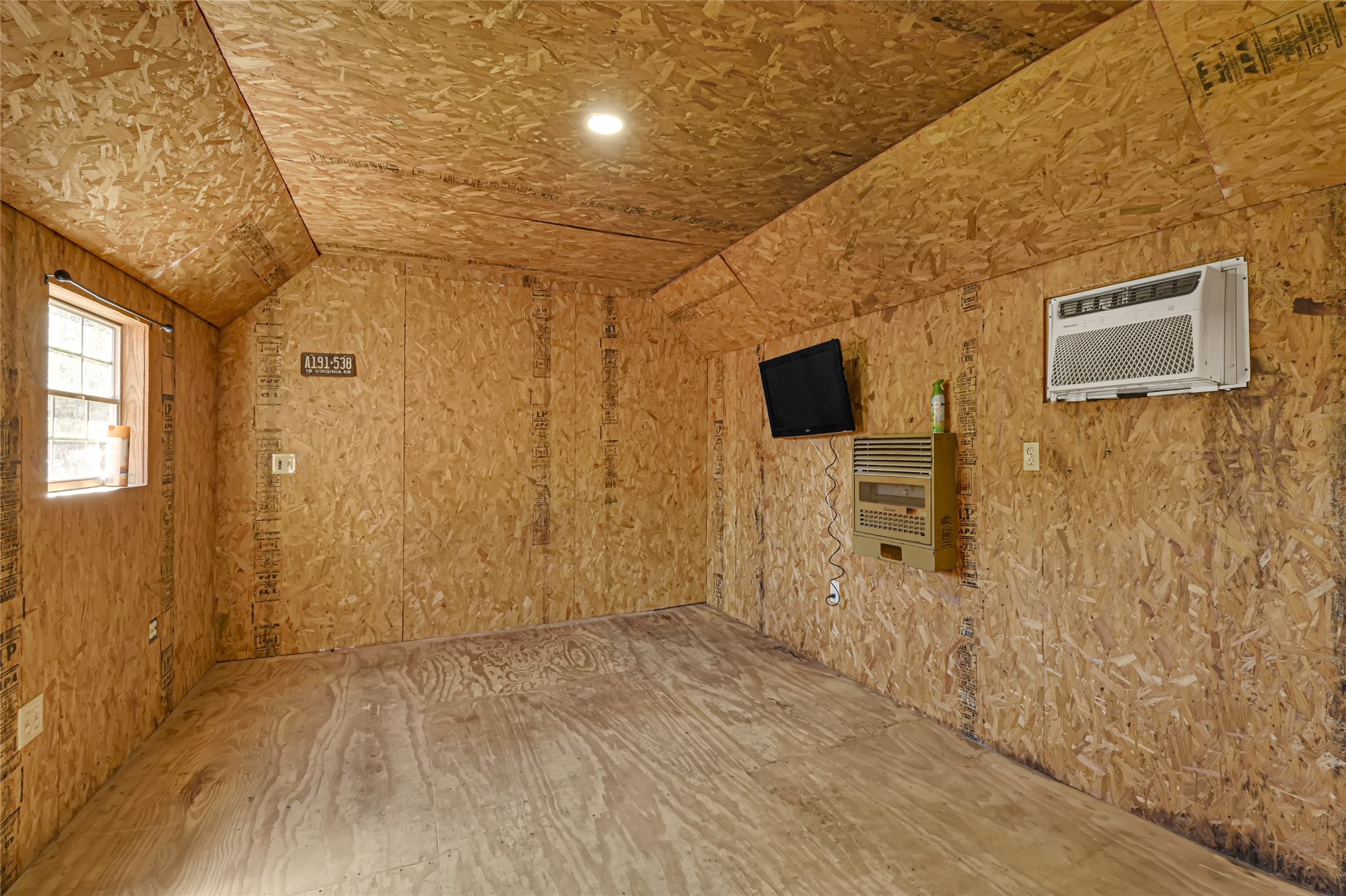 Cozy and versatile room with natural wood paneling, featuring a window for ample daylight, wall-mounted air conditioning, and heating unit for year-round comfort.