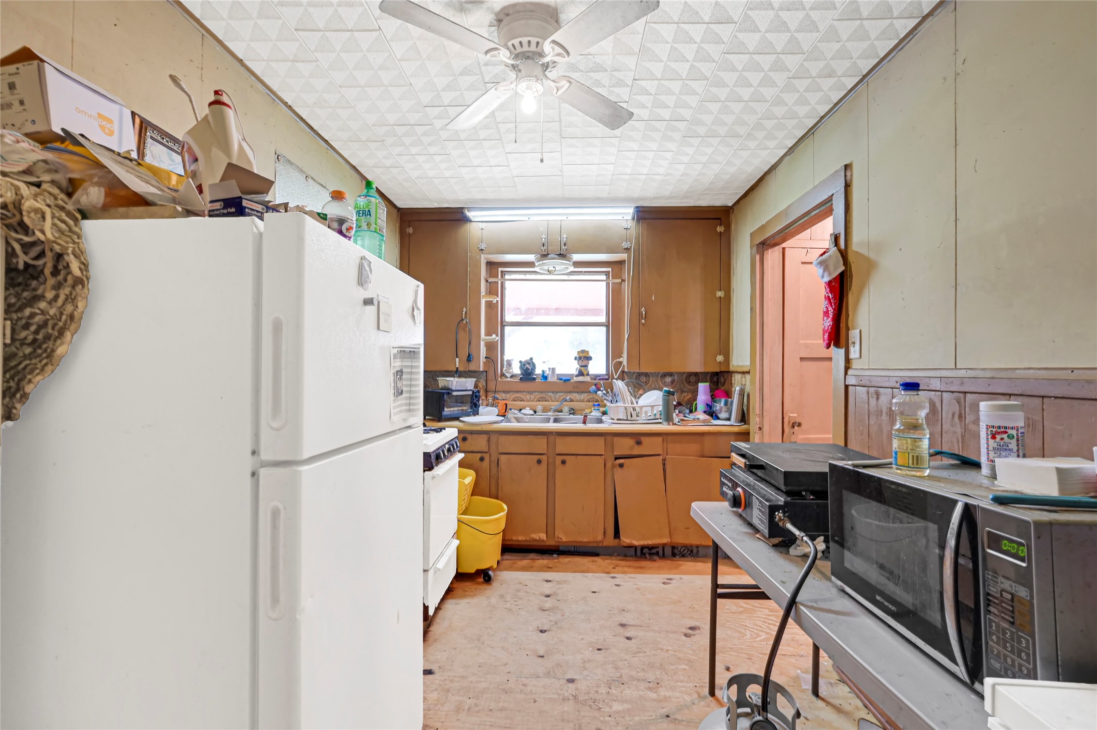 Cozy kitchen with ample cabinet space, featuring a ceiling fan and natural light from a central window, offering potential for customization.
