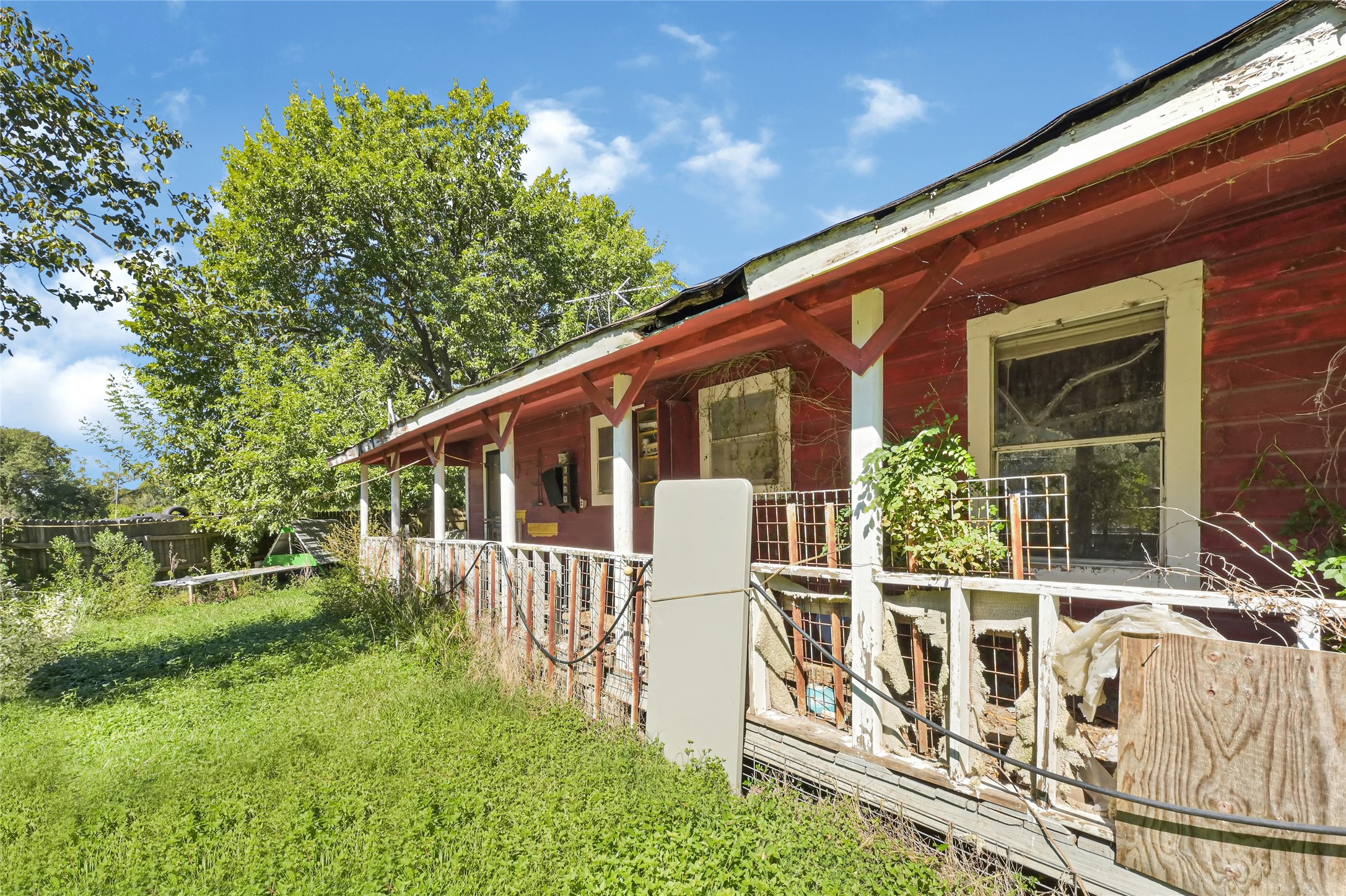 Charming rustic home with a classic red exterior and spacious wrap-around porch, set amidst lush greenery. Perfect for those seeking a renovation project with character.