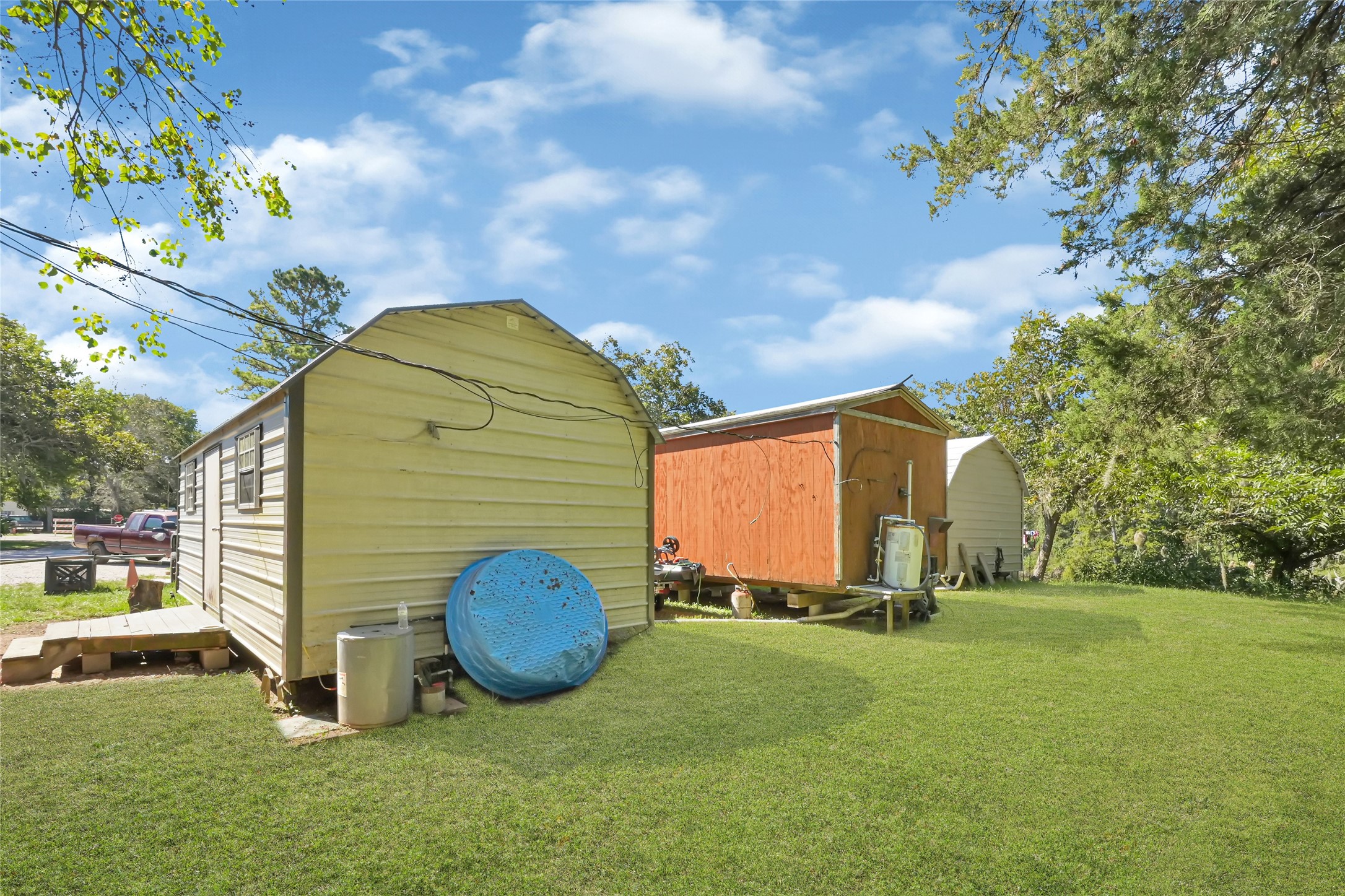 Spacious backyard with multiple storage sheds, surrounded by mature trees for added privacy and shade.