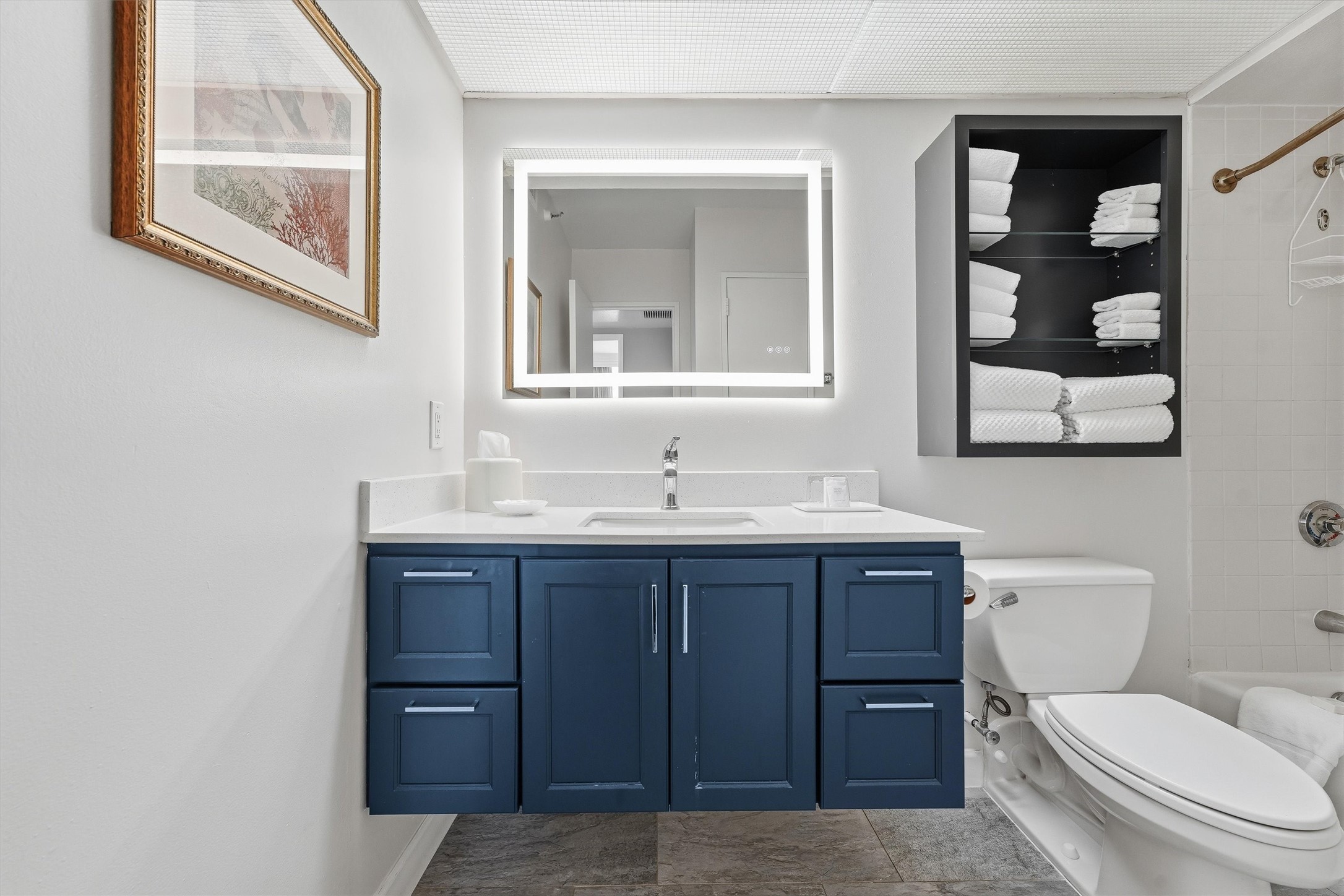 A colorful vanity adds a stylish contrast, while drawers and open shelving provide convenient bathroom storage.