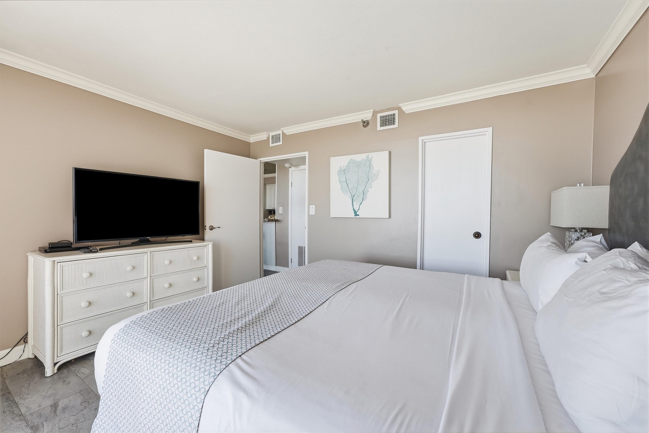 Soft neutral tones, crown molding, and tile flooring create a restful bedroom retreat after a day at the beach.