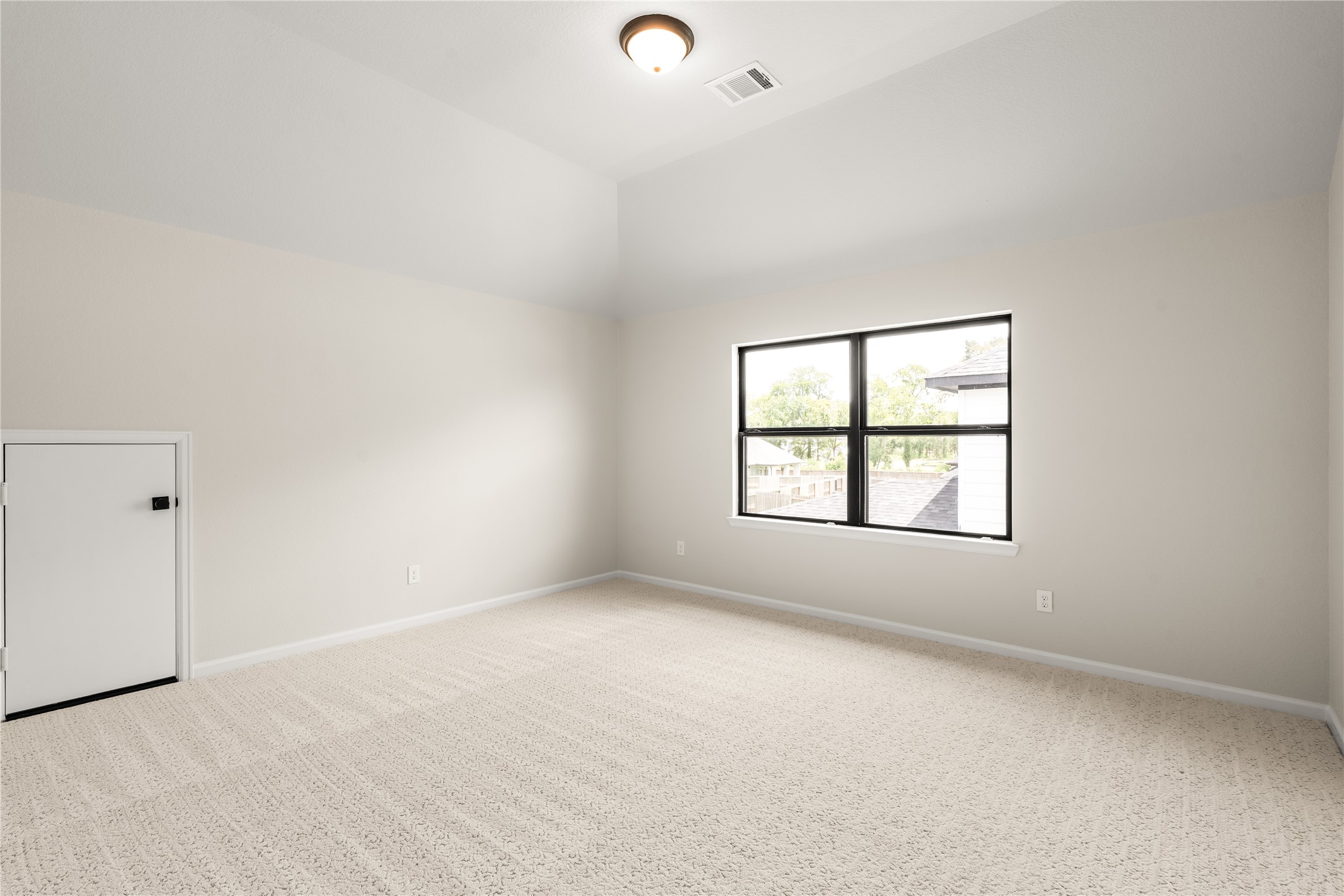 Spacious, light-filled room with plush carpeting, high ceilings, and a large window.
