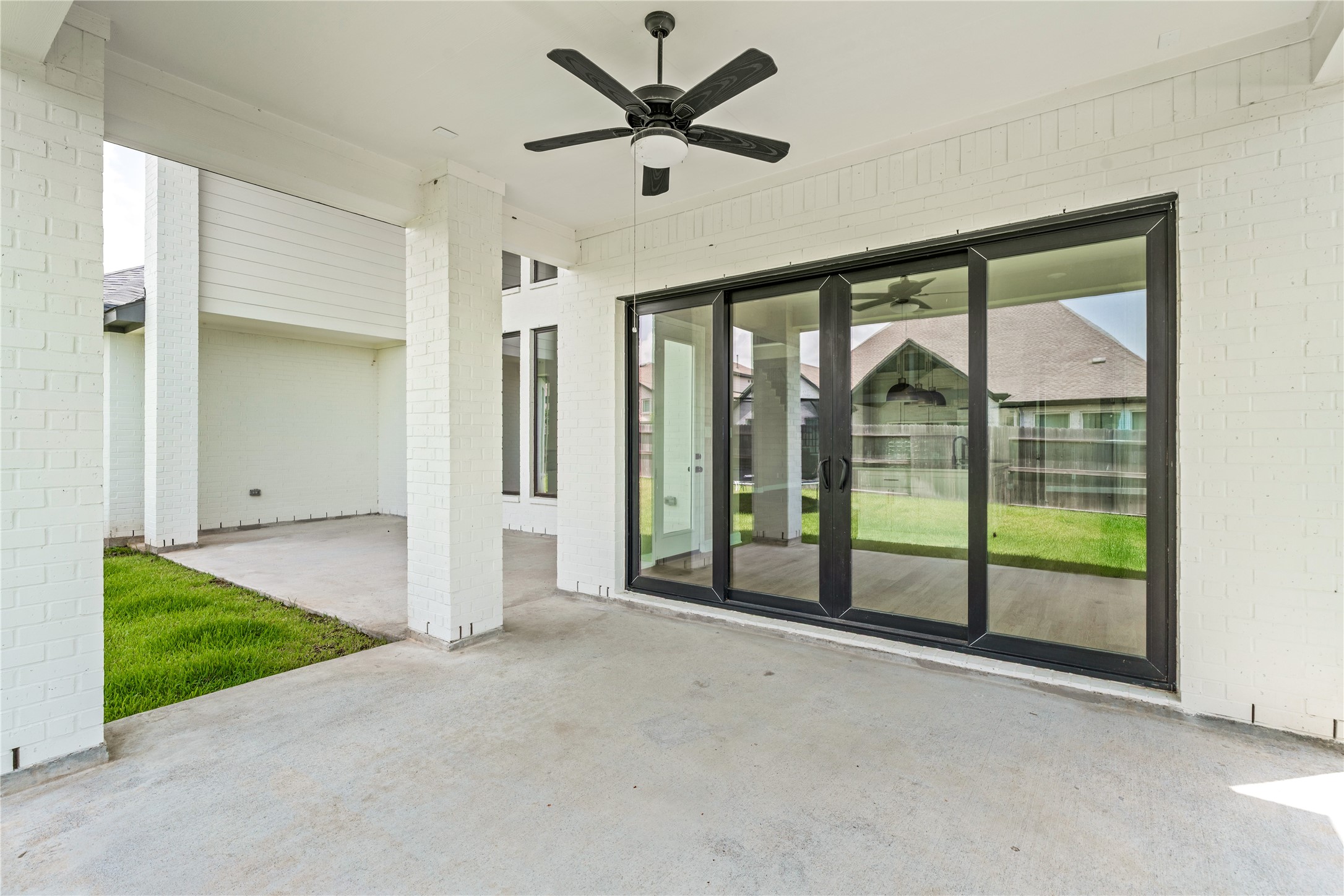 Spacious covered patio with modern ceiling fan and expansive sliding glass doors, perfect for seamless indoor-outdoor living.