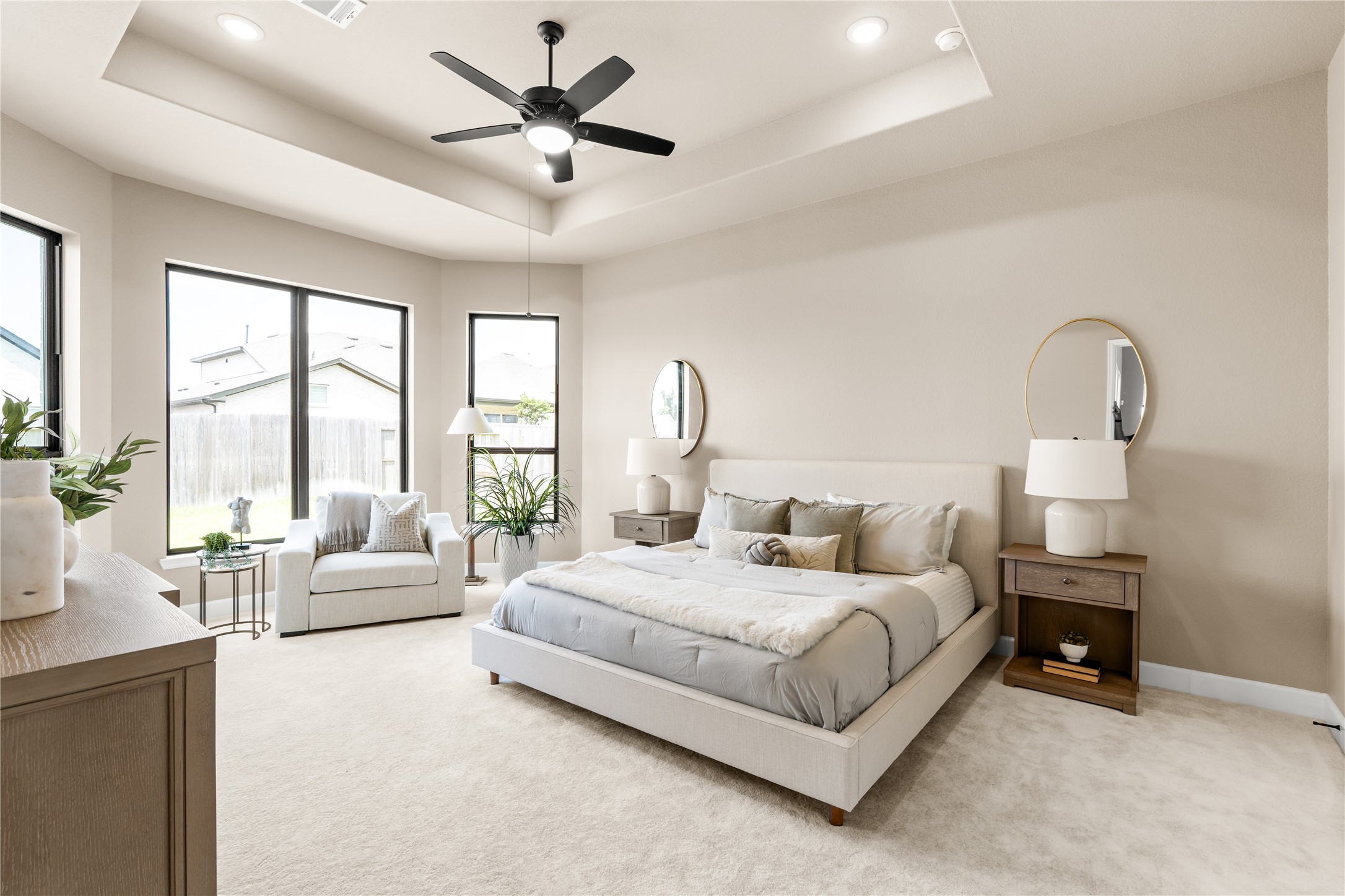 Welcome home to your sunlit primary bedroom featuring a tray ceiling, modern ceiling fan, and large windows overlooking the backyard. *Virtually Staged*