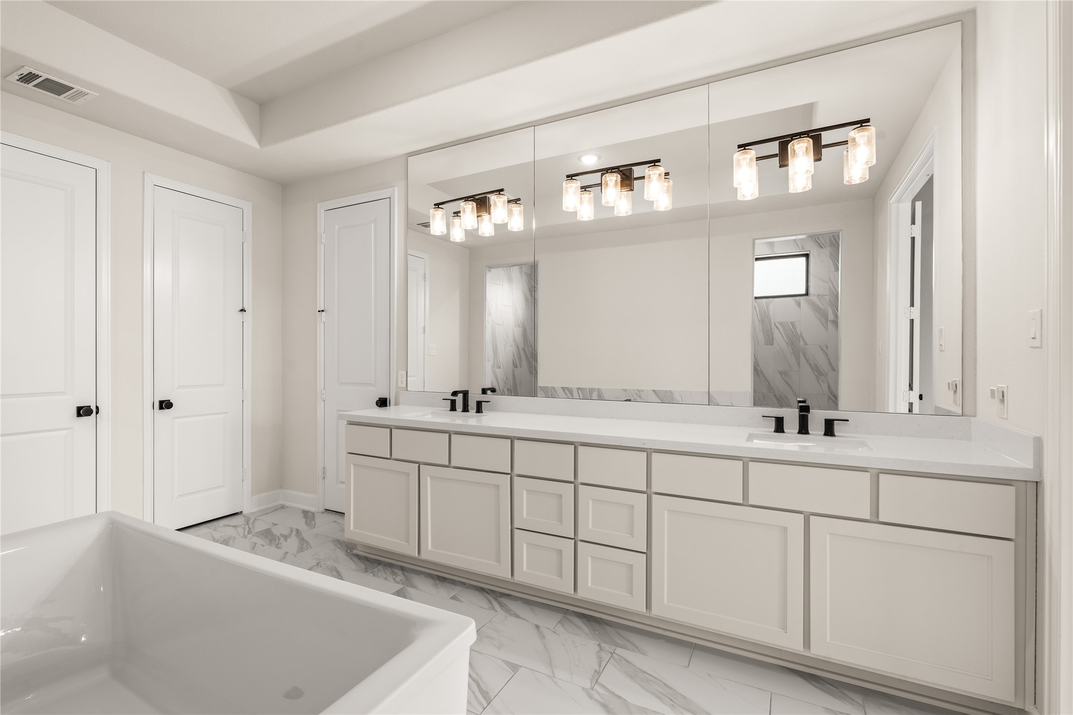 Splendid primary bathroom featuring a spacious double vanity with modern fixtures, elegant lighting, and ample cabinetry, all set against a backdrop of marble flooring.