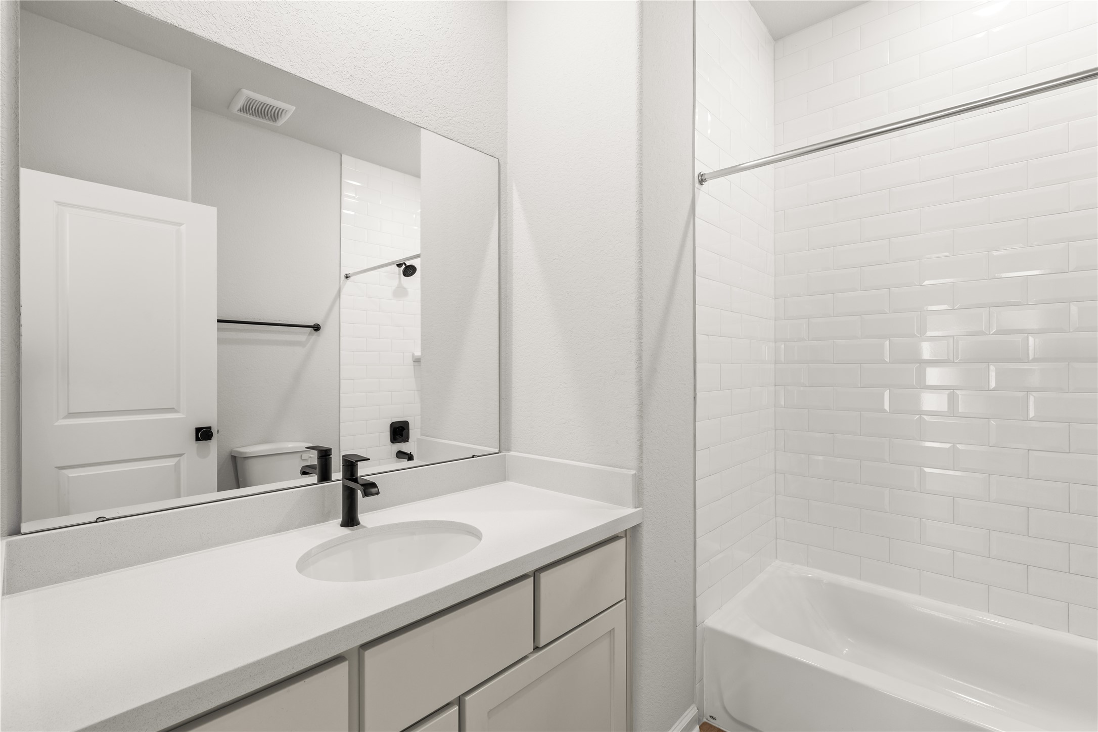 Modern bathroom showcasing a sleek vanity with a black faucet, elongated mirror, and a pristine white-tiled bathtub.