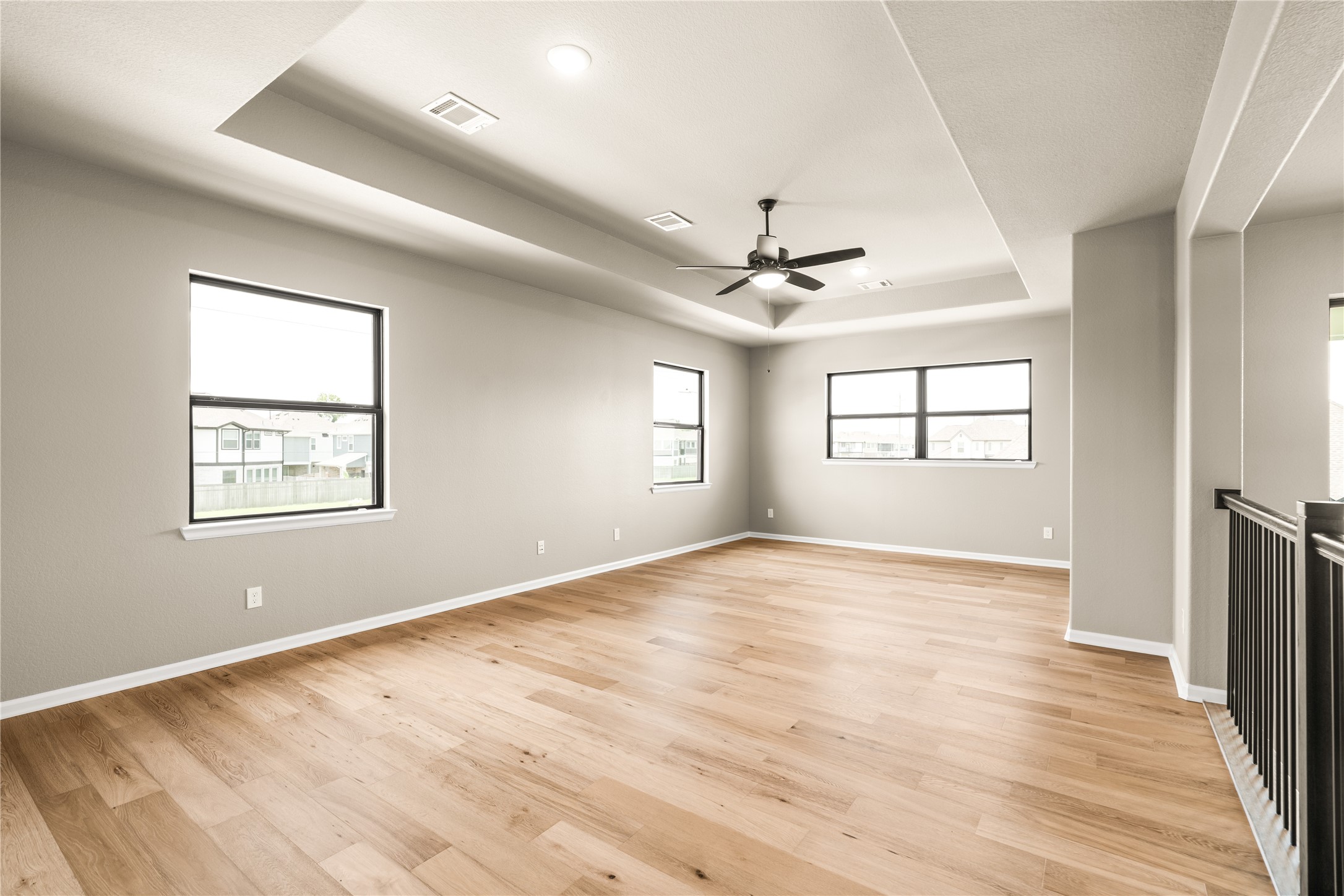 Spacious and bright loft /gameroom area with elegant wood flooring, a modern ceiling fan, high ceiling, and a plethora of windows that invite natural light.