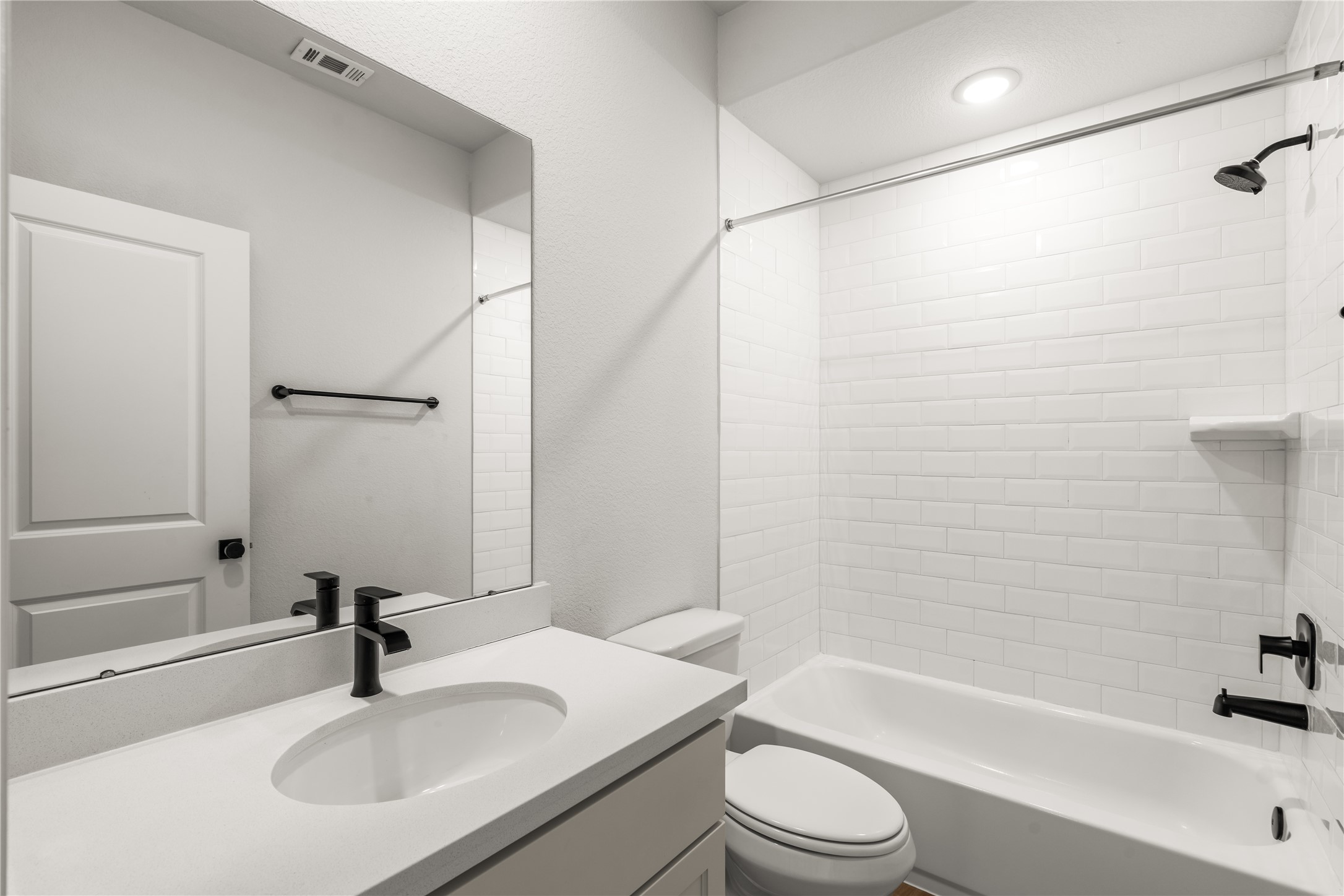 Secondary bathroom featuring a modern vanity with a black faucet and a pristine white subway tile shower with matching black fixtures.