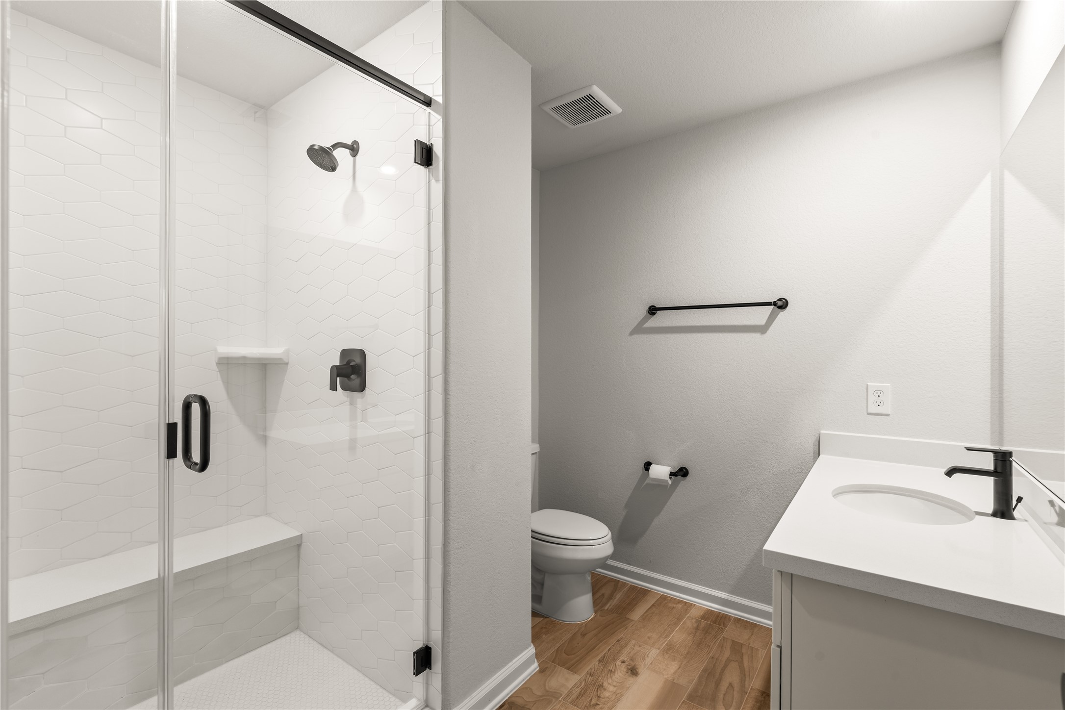 Modern bathroom featuring a sleek glass-enclosed shower with stylish fixtures, a pristine vanity, and elegant wood flooring.