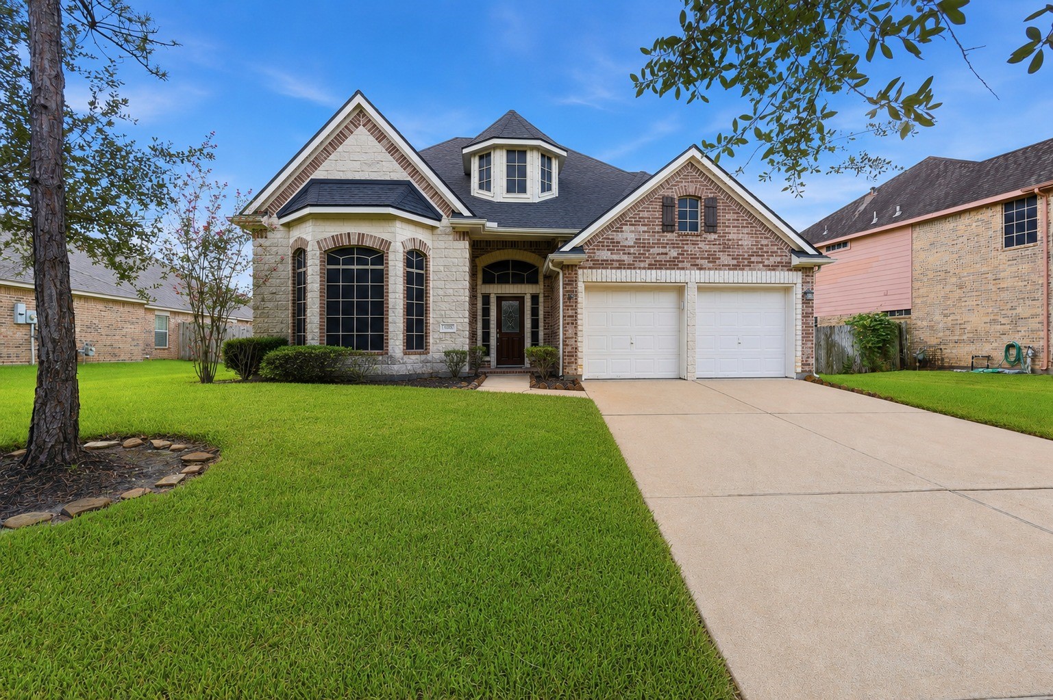 An impressive 4-bedroom, 3.5-bath home in Savannah Cove, 13806 Cove Landing Lane showcases a striking brick-and-stone exterior, mature trees, and inviting curb appeal.