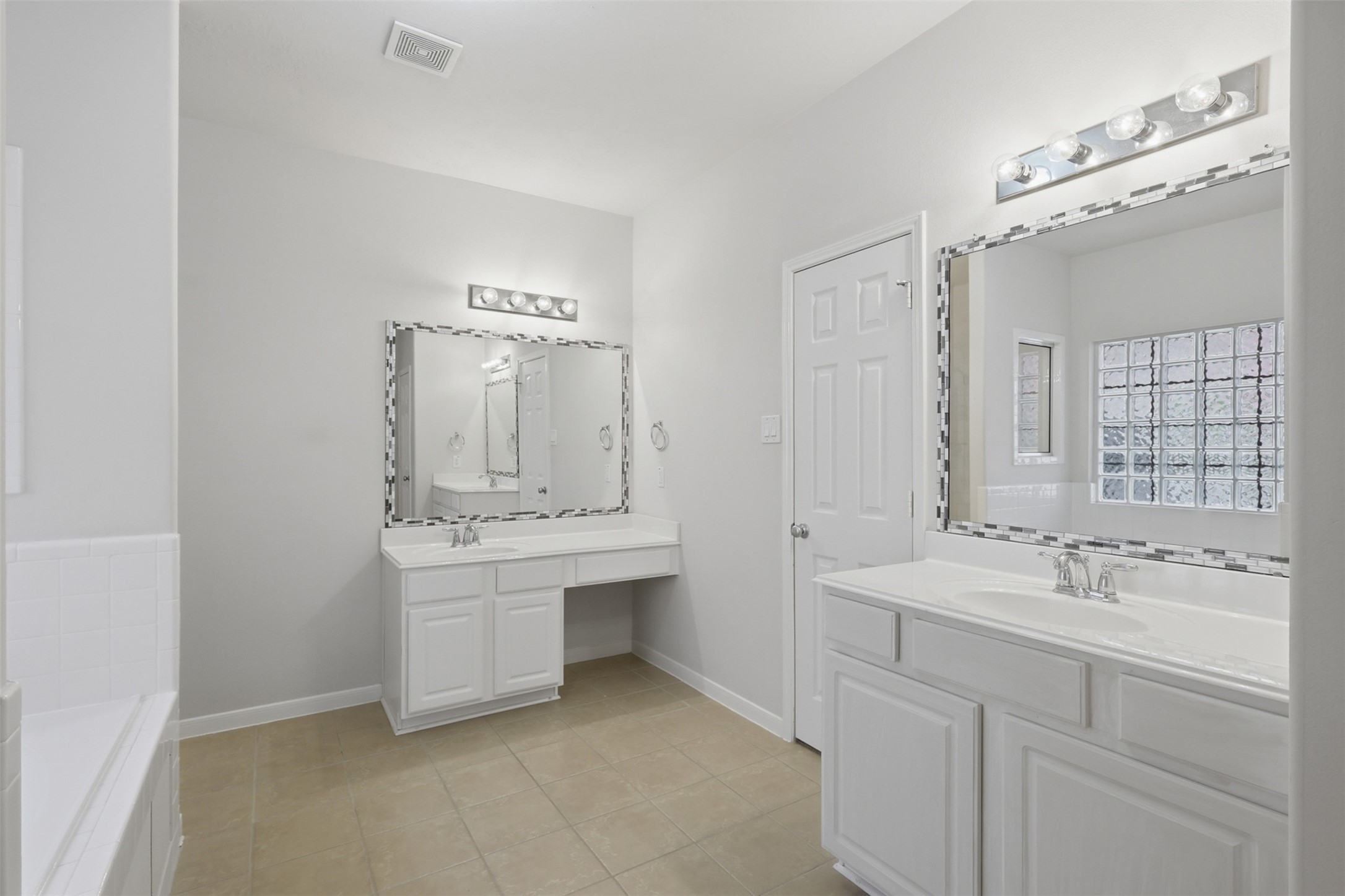 The primary bath offers separate vanity areas, ample storage, tile flooring, and a bright, functional layout.