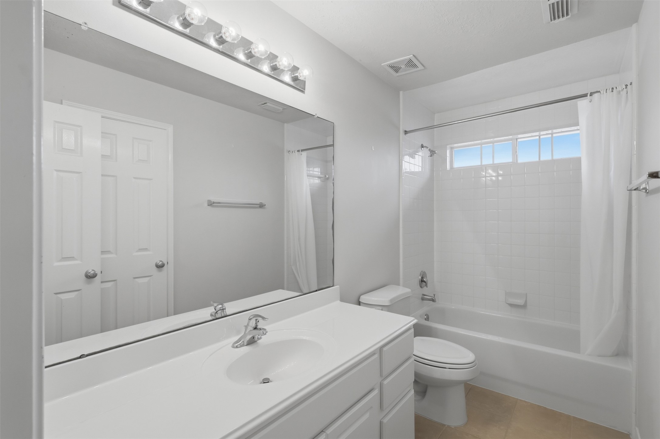 This full secondary bath includes a spacious vanity, tub-and-shower combination, and natural light from the transom window.