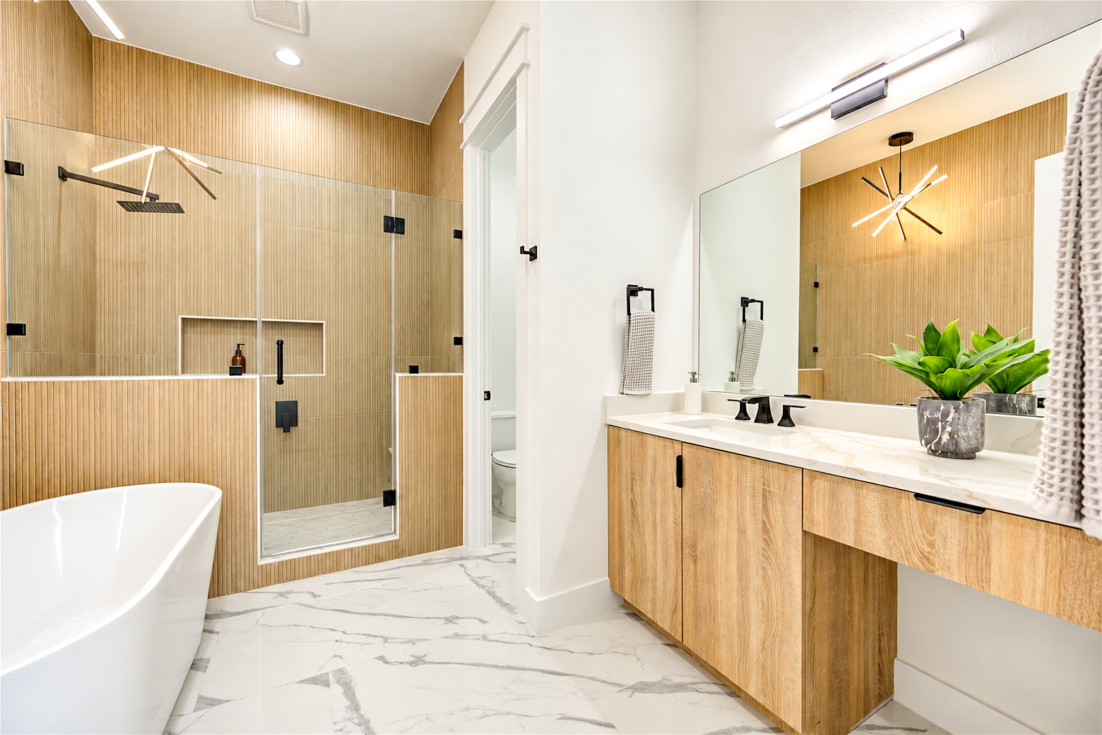 Primary bath with a freestanding tub, glass-enclosed rain shower, and vanity with a makeup area.