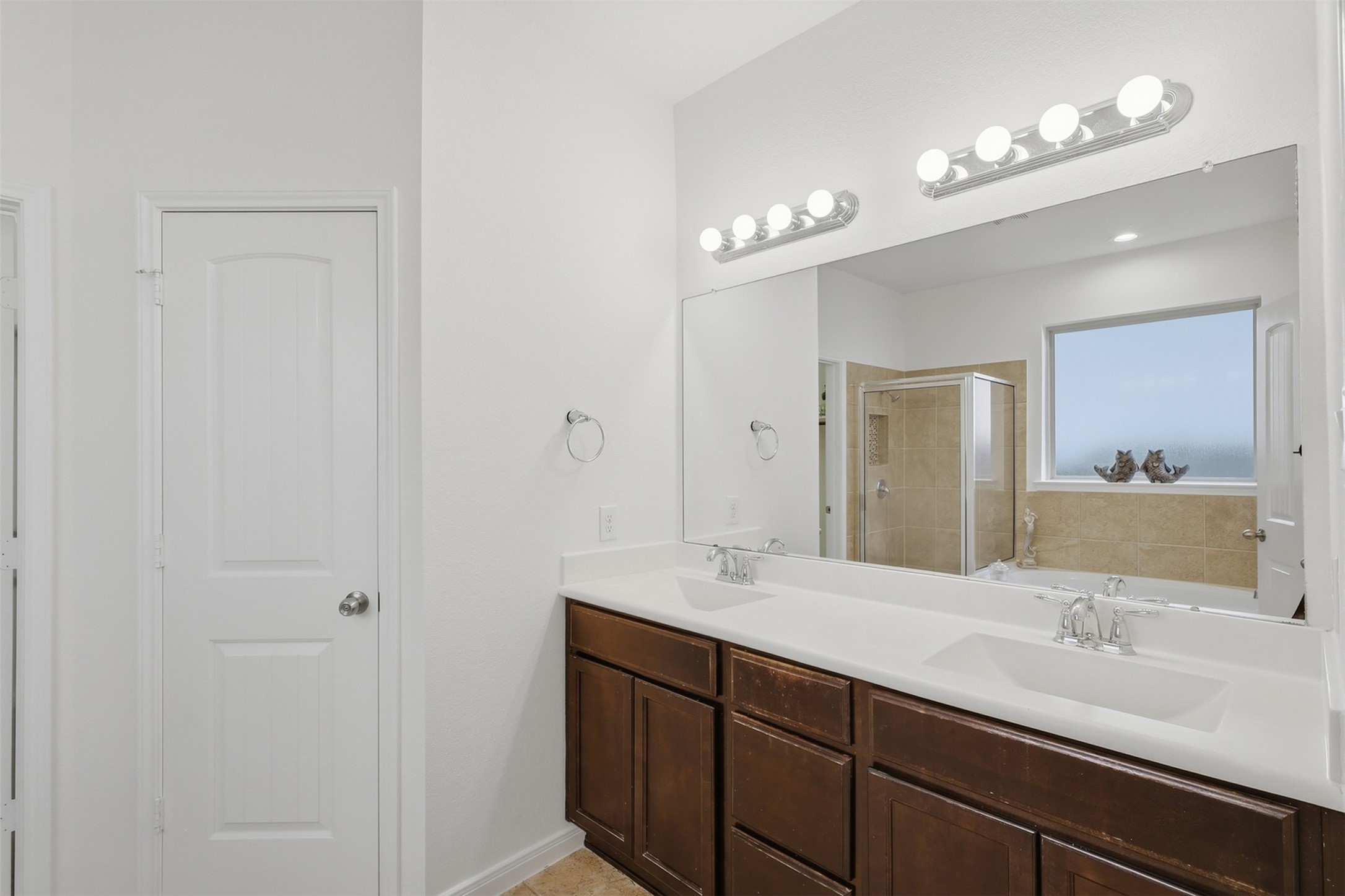 Beautifully Finished Primary Bath! The spacious double vanity offers plenty of counter space and storage, complemented by elegant lighting and a large mirror. The warm cabinetry and bright finishes create a clean, comfortable space that is both practical and inviting.