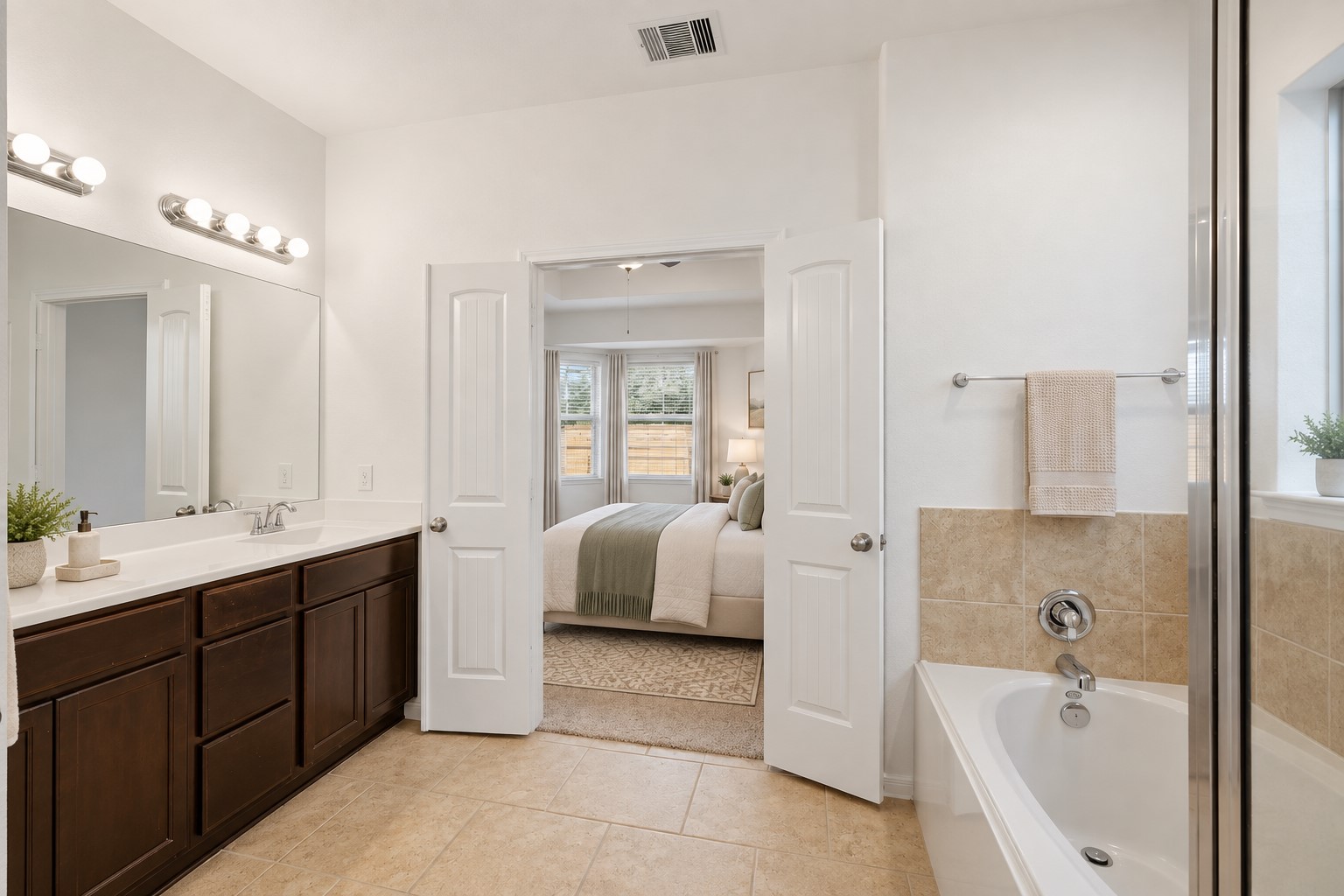 A Lovely Spa-Inspired Primary Bath! The spacious primary bath features a beautiful double vanity, generous mirror, soaking tub, separate glass-enclosed shower, and warm tile flooring. The bright, clean design creates a relaxing atmosphere and provides plenty of room to start the morning or unwind at the end of the day. *Photo is virtually staged*