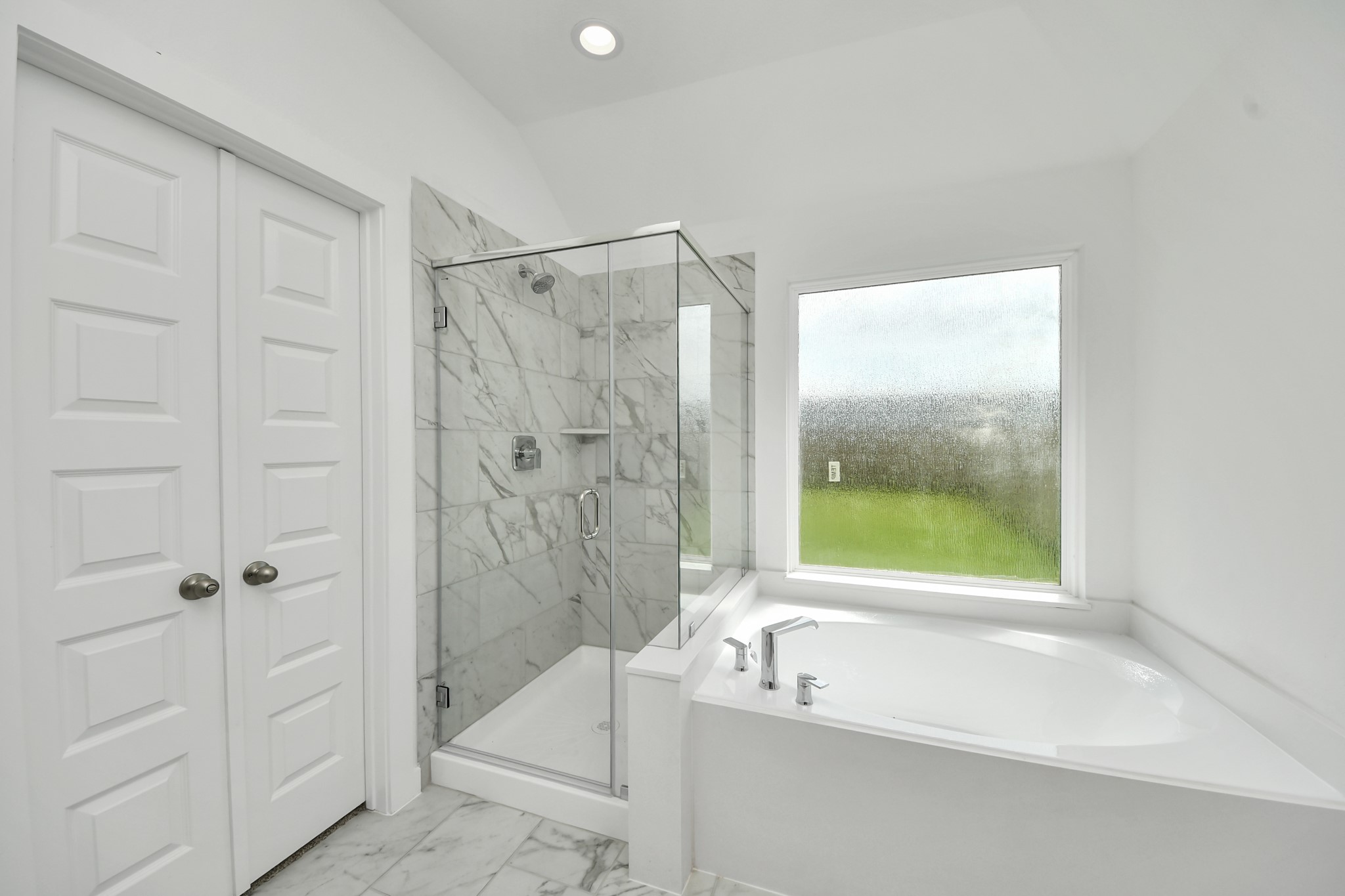 Escape to a spa-like oasis in this primary bathroom. Enjoy a walk-in shower with tile surround, a separate garden tub with custom detailing, and an elegant vanity featuring light countertops, modern hardware, and beautiful vanity lights. Experience luxury and relaxation in every detail. Sample photo of completed home with similar floor plan. Actual colors and selections may vary.